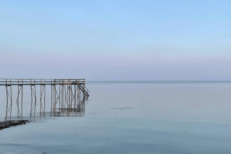 Pier jutting into calm Lake Winnipeg with blue sky.