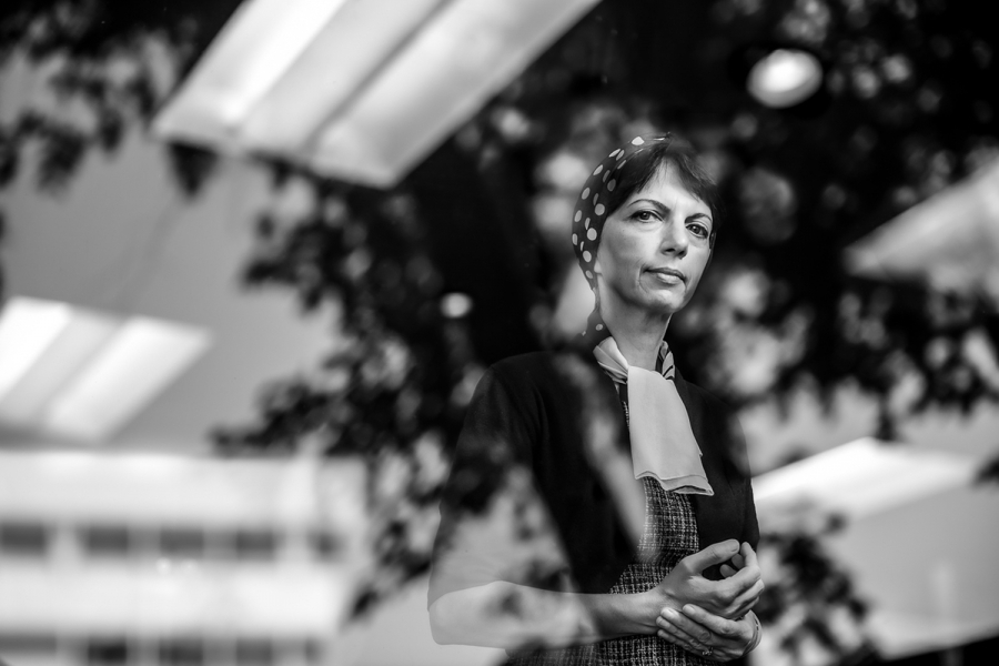 Zahra Moussavi stands at reflected window with a pensive look on her face. Blurred trees can be seen in the windows reflection.