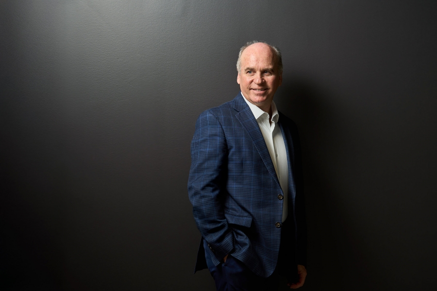 A press shot of a man with short grey hair (Dave Angu) in a blue suit, smiling