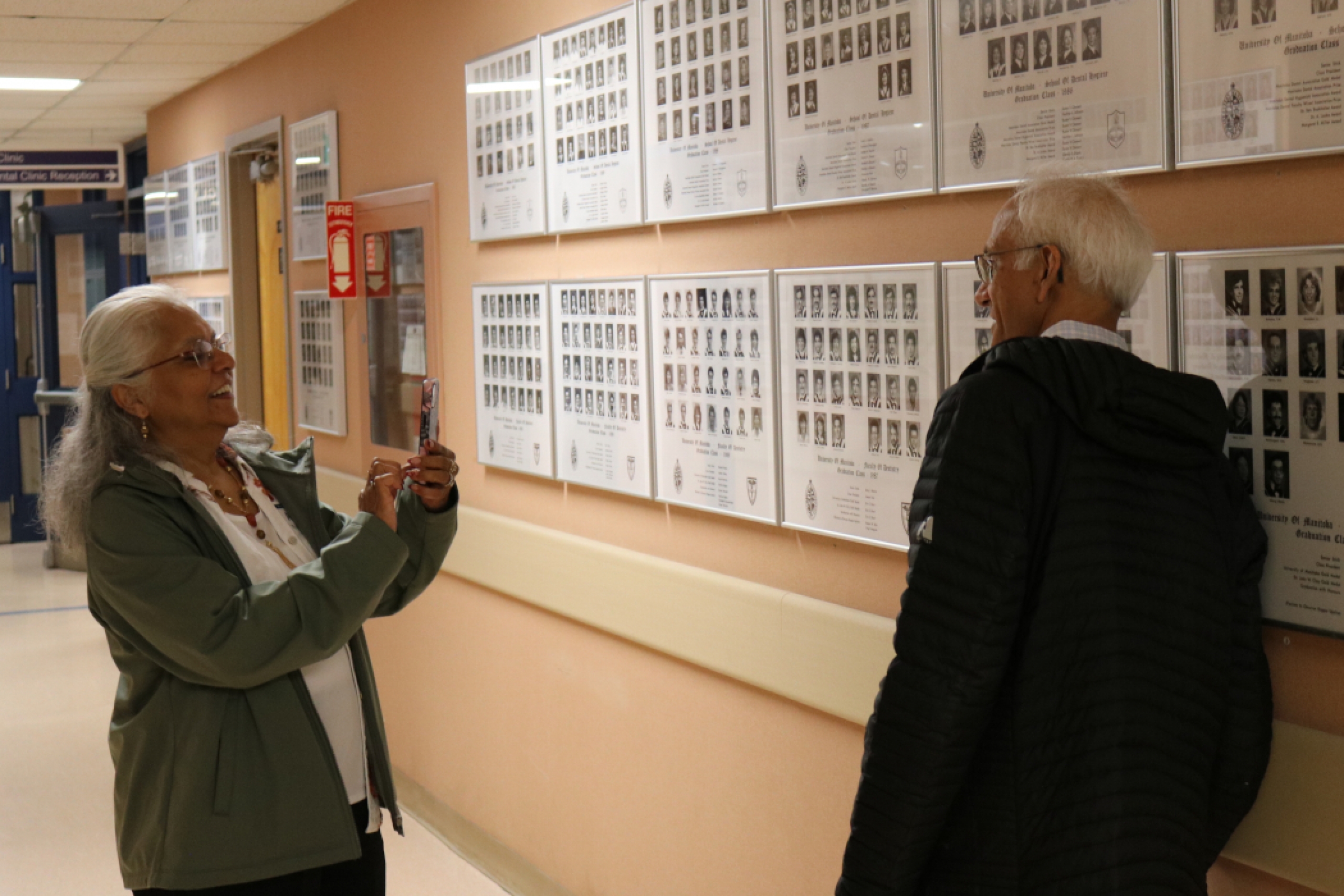 A person takes a photo of another person standing in front of dentistry graduation photos. 