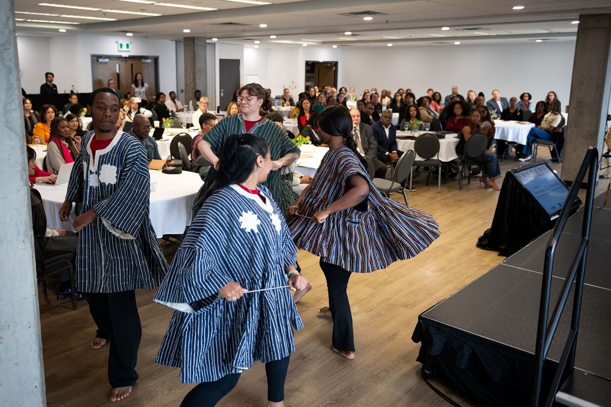 Four Black dancers in traditional dress dancing for meeting attendees.