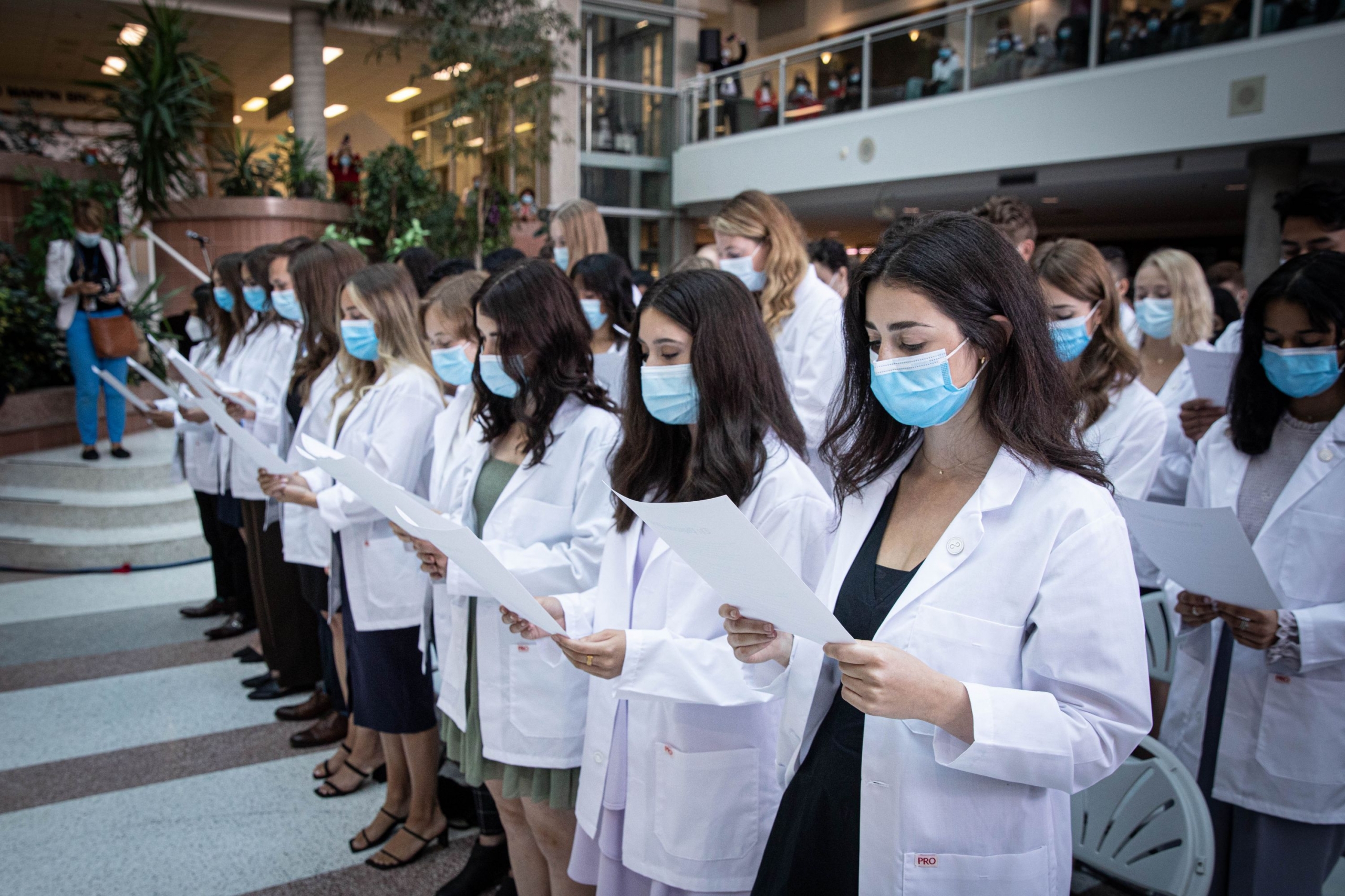 First-year medical students wearing white coats stand to read and recite the Physician's Pledge.