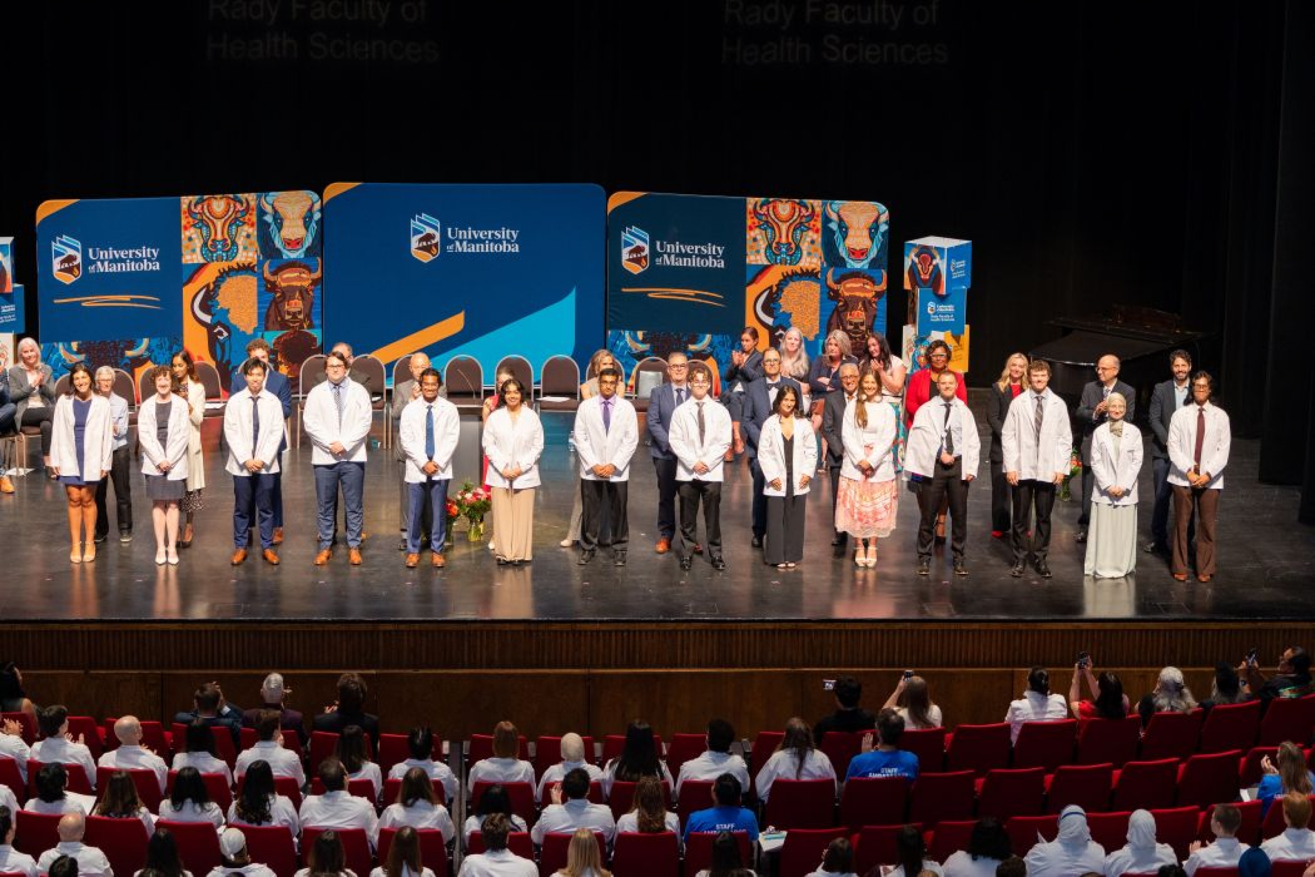 Students stand on stage after putting on their white coats. 