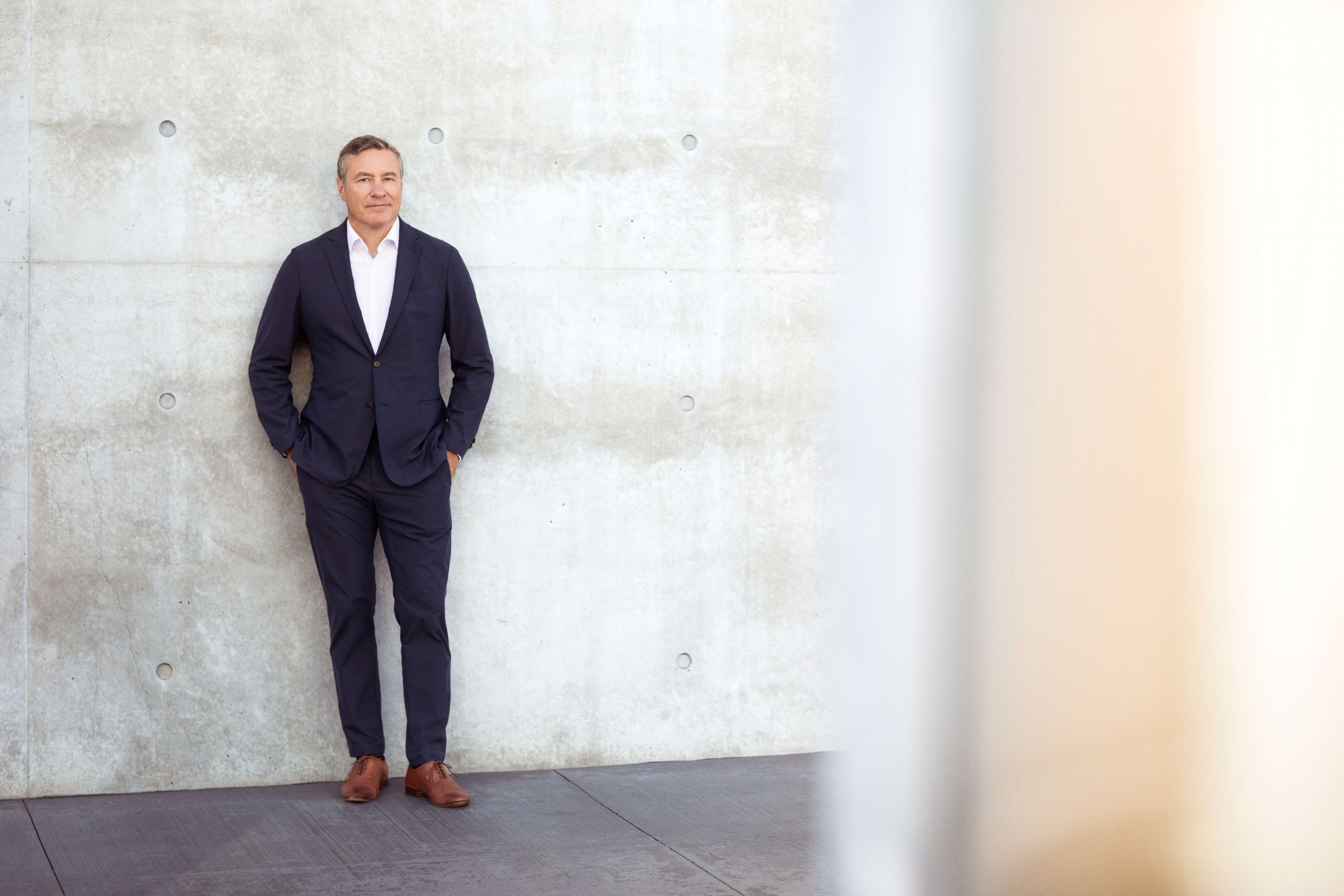 A man in a suit by a concrete wall