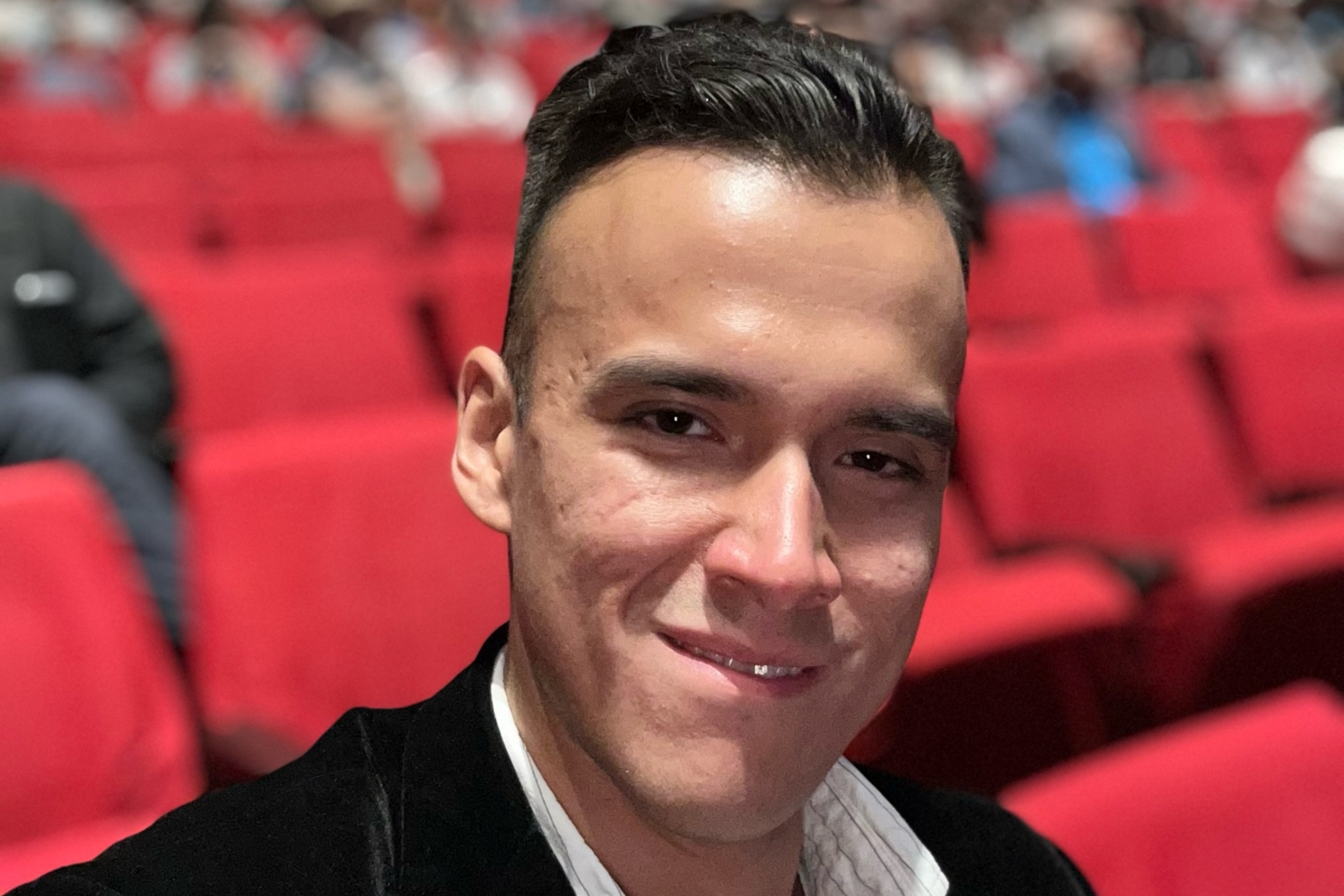 A man in a black blazer smiles for photo while seated.