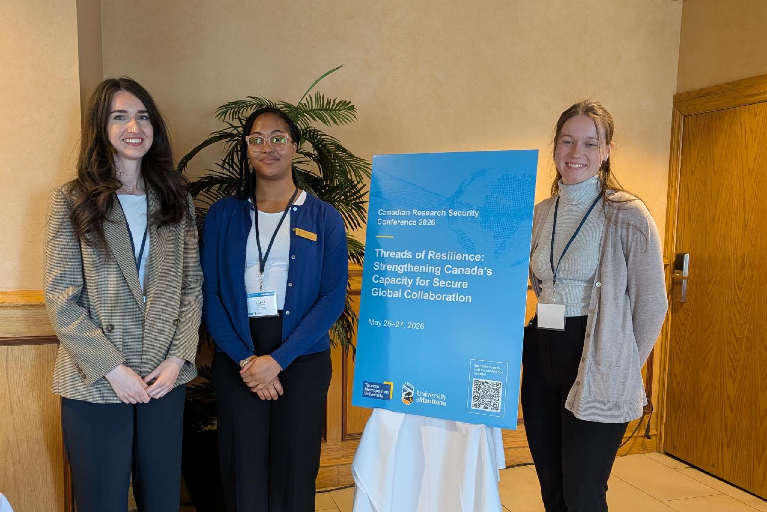 Three conference attendees standing beside a Canadian Research Security Conference 2026 sign in an indoor venue.
