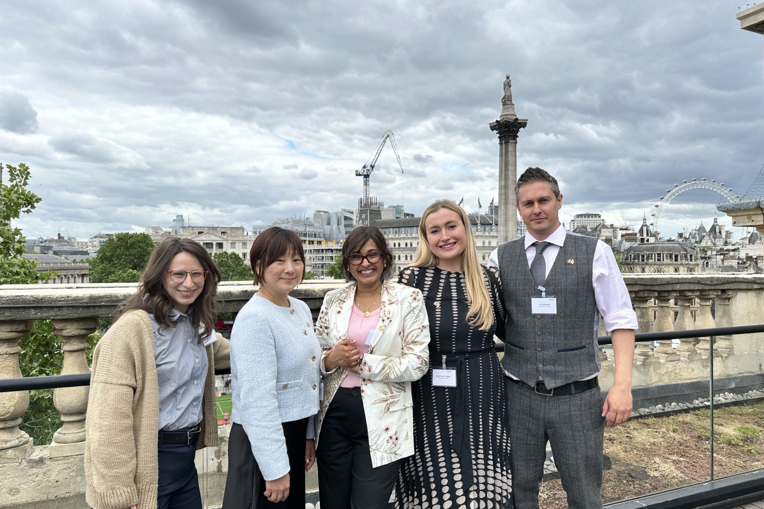 Five conference attendees smiling together on a rooftop terrace overlooking Winnipeg on a cloudy day