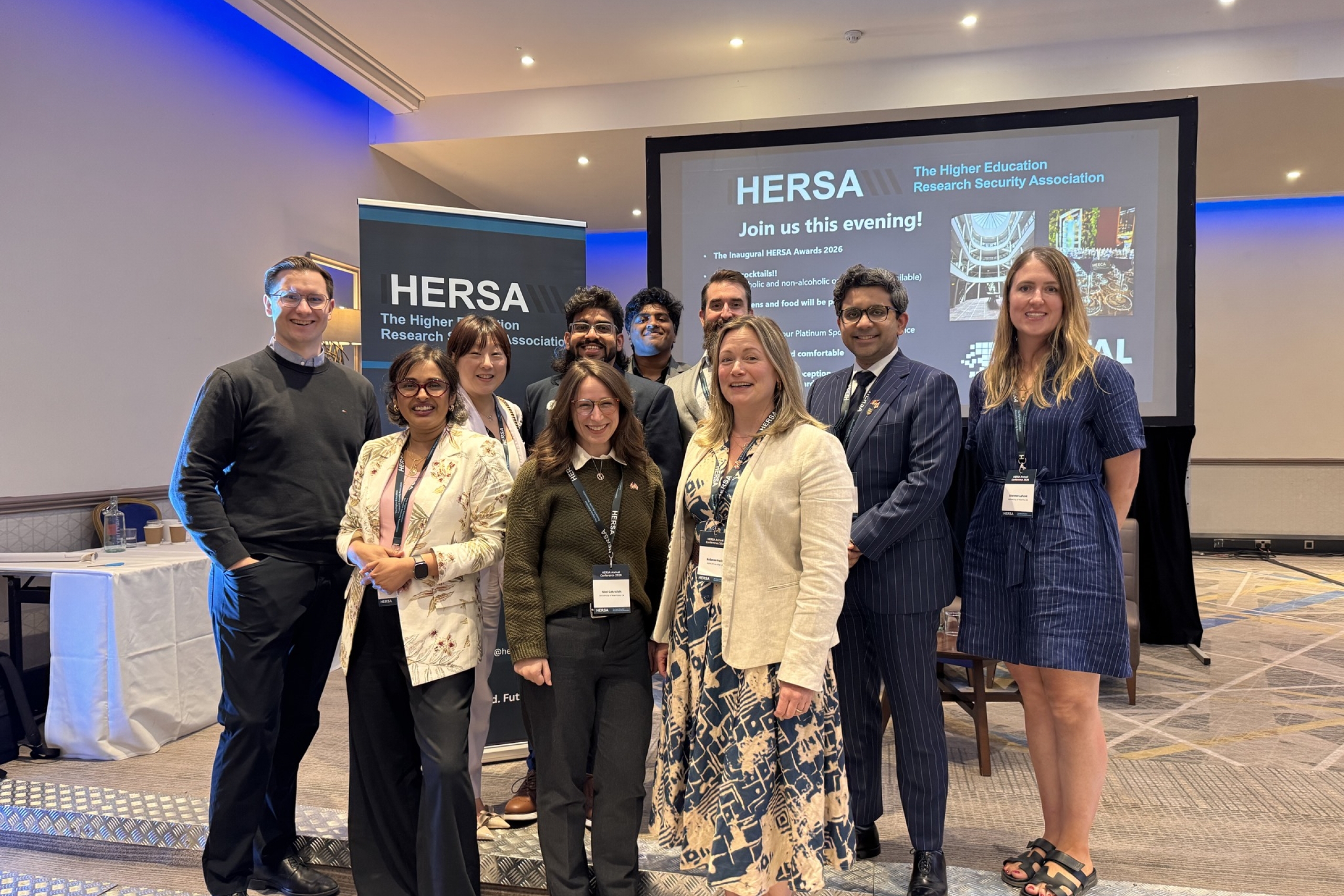 HERSA conference attendees smiling together in front of event signage and a presentation screen.