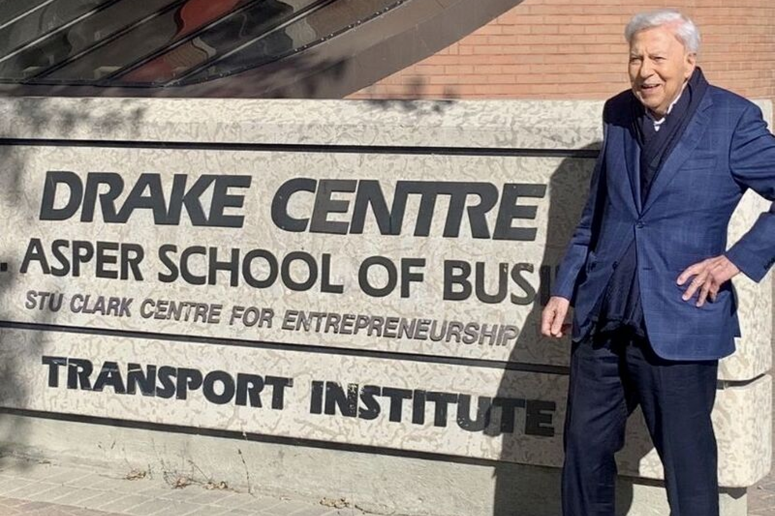 A man in blue suit standing outside a building with his name on it.