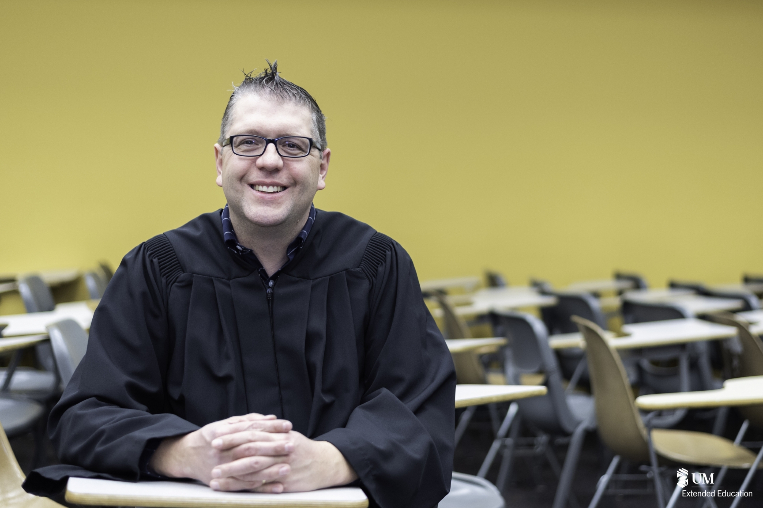 Grad in gown sitting at a desk in classroom