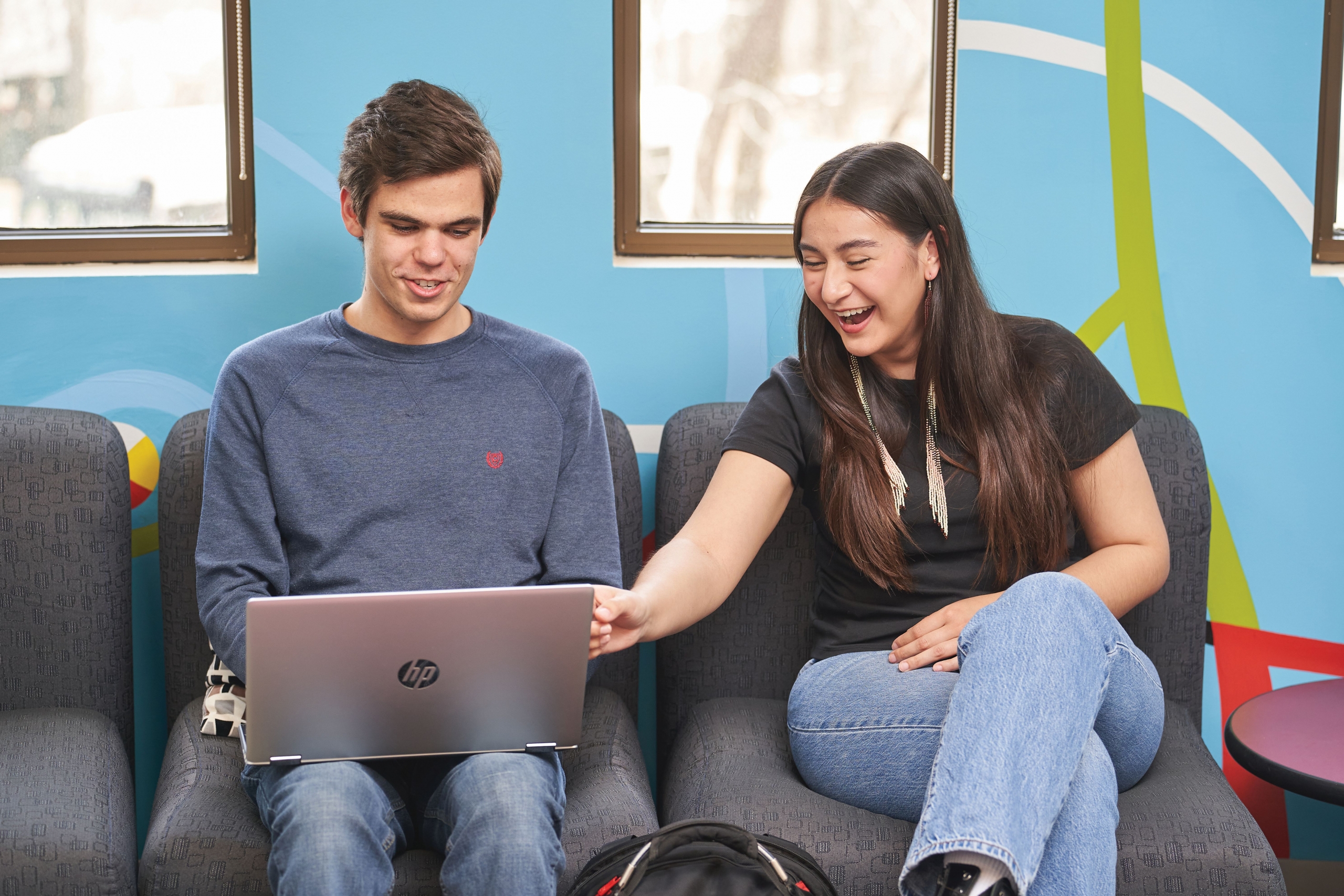 Students look at a laptop while smiling