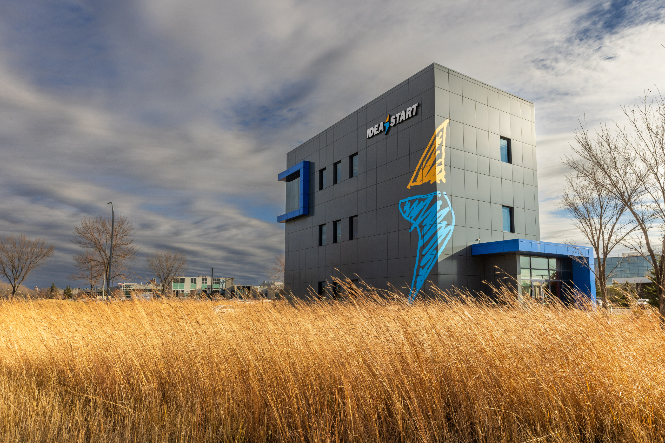 IDEA START building at the University of Manitoba, set against prairie grass and a cloudy sky