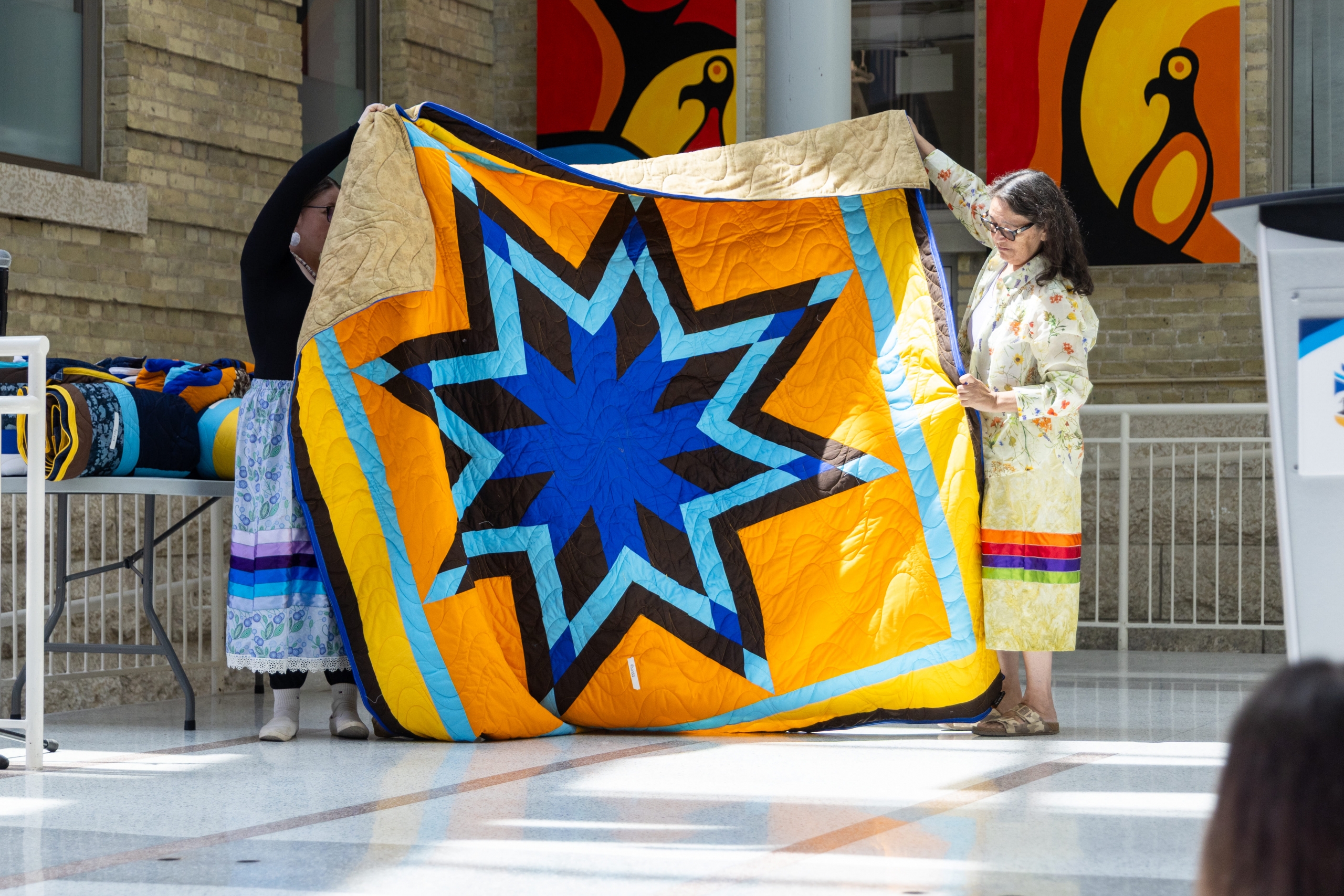 golden yellow and blue star blanket held by two women, being presented.