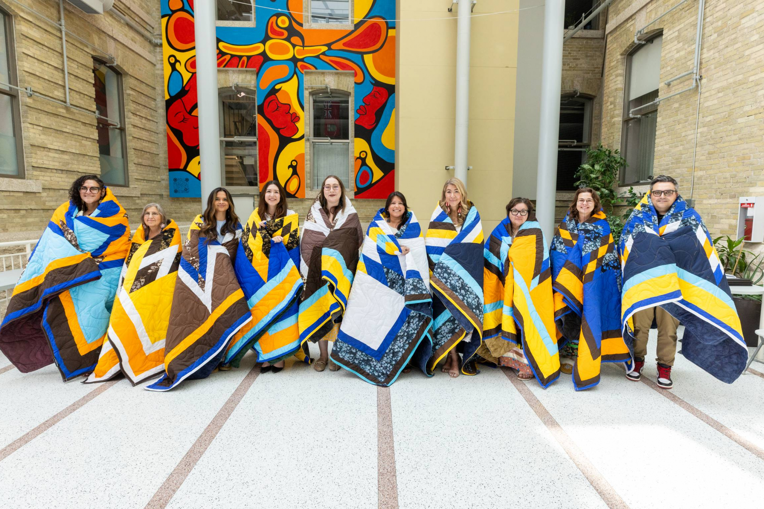 Ten individuals stand on a stage wrapped in star blankets.