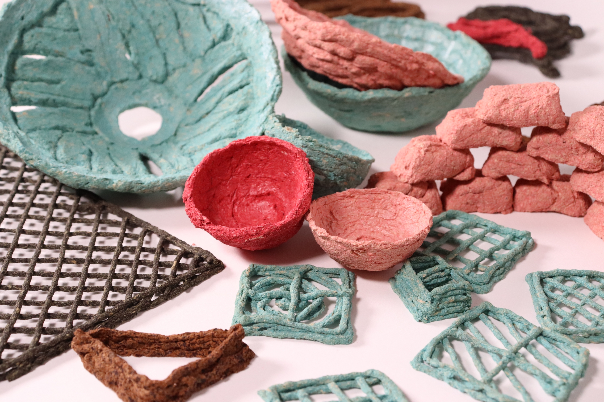 Textured, eco-friendly bowls and geometric shapes in teal, red, and brown hues are arranged on a surface, conveying a handcrafted, sustainable feel.