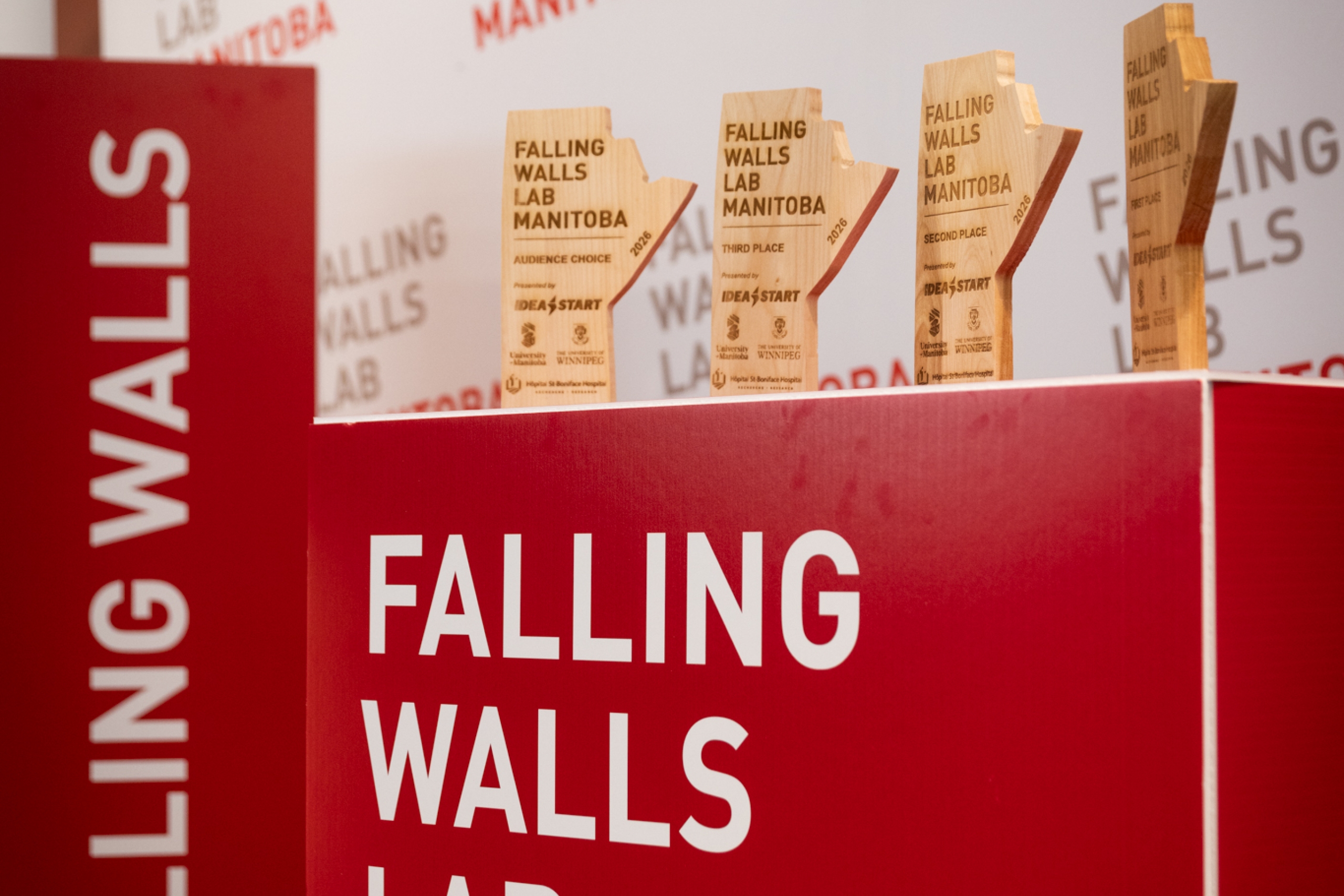 Wooden Falling Walls Lab Manitoba 2026 trophies displayed on a red event stage.