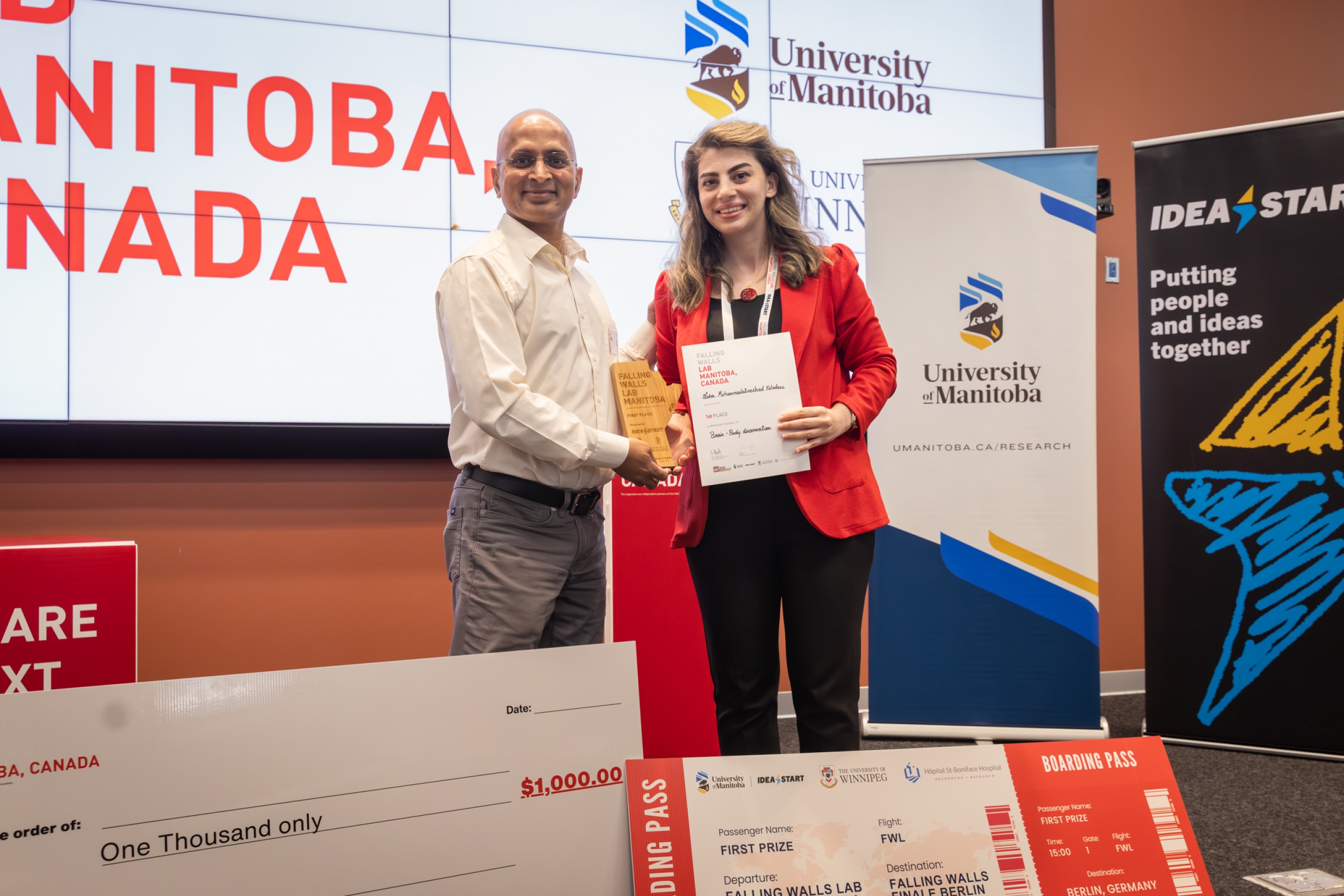 Dr. Saba Mohammadalinezhad Kolahdouz stands with an award presenter, holding her first place certificate and trophy at Falling Walls Lab Manitoba 2026.