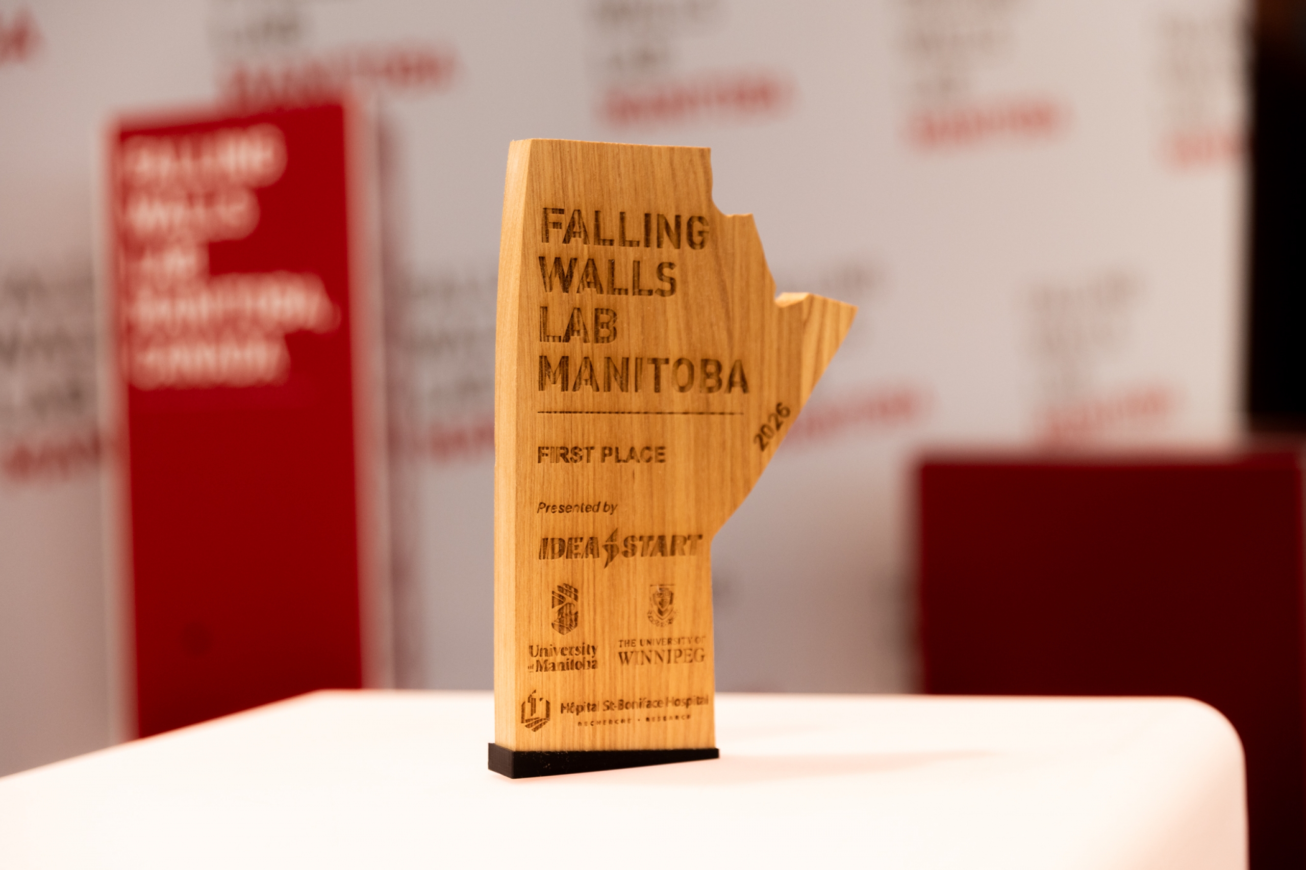 A wooden Falling Walls Lab Manitoba 2026 first place trophy displayed on a white table.
