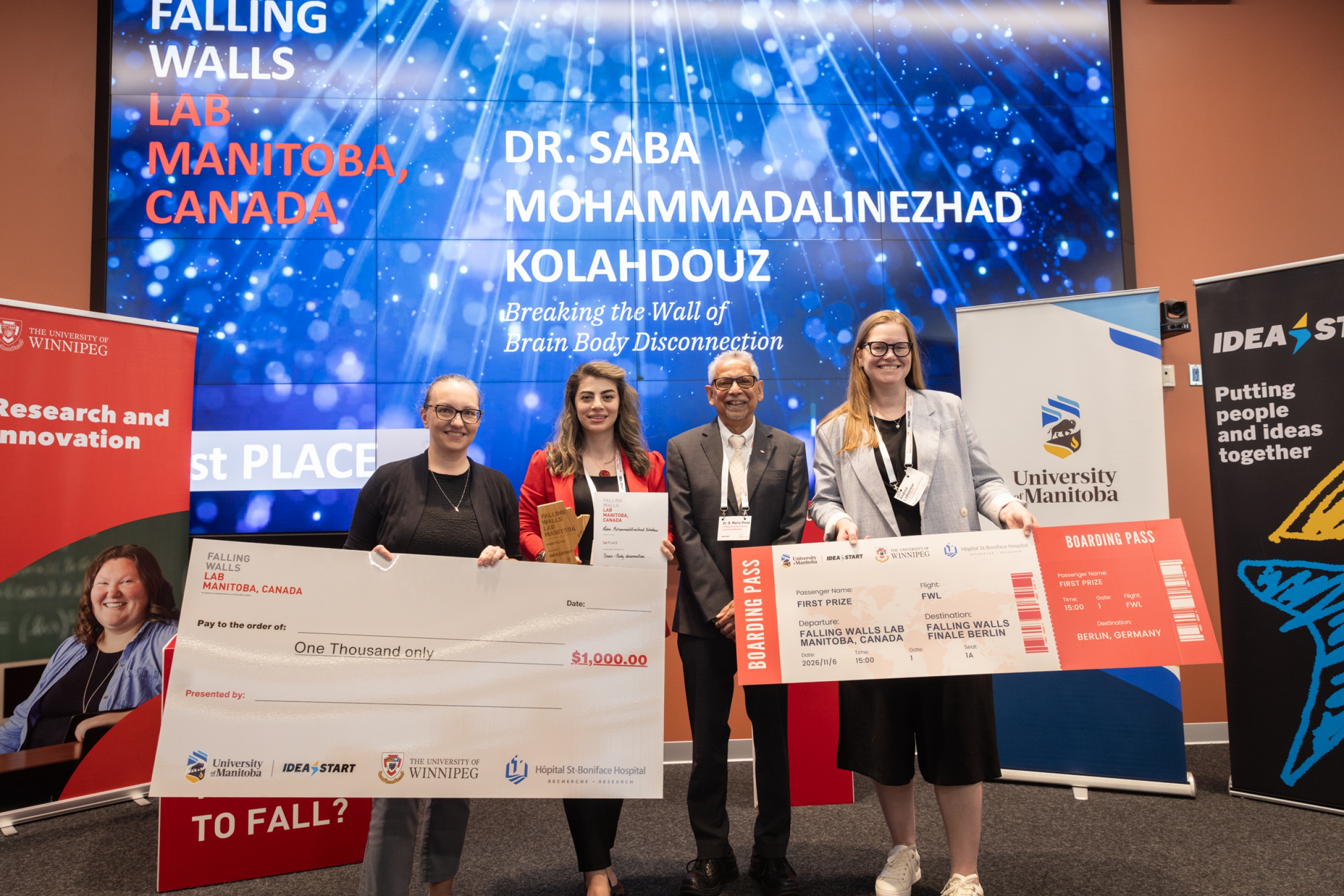 Dr. Saba M. Kolahdouz stands with award presenters, holding her first place certificate and trophy at Falling Walls Lab Manitoba 2026.