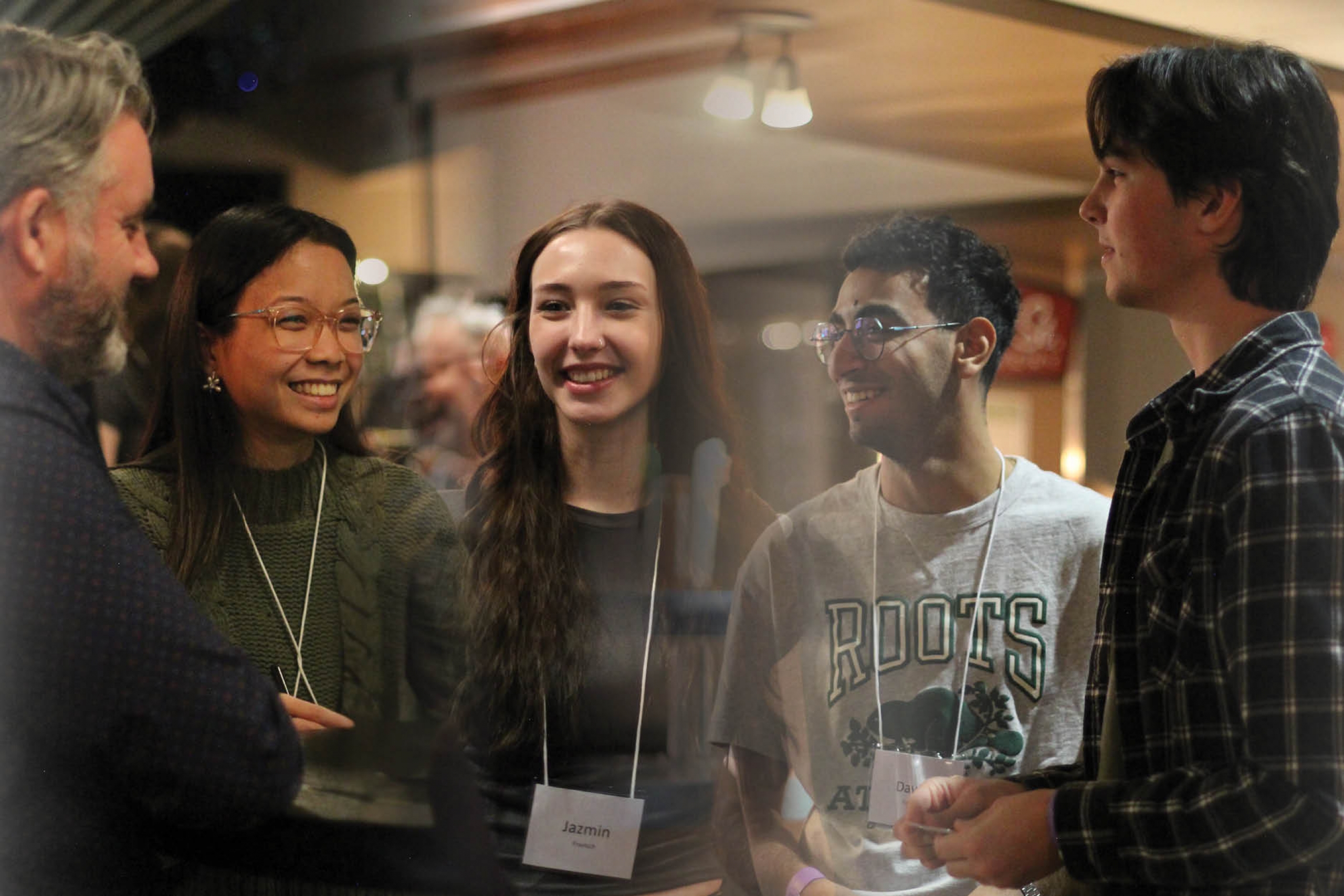 A group of five people stand close together indoors, smiling and engaged in conversation. 