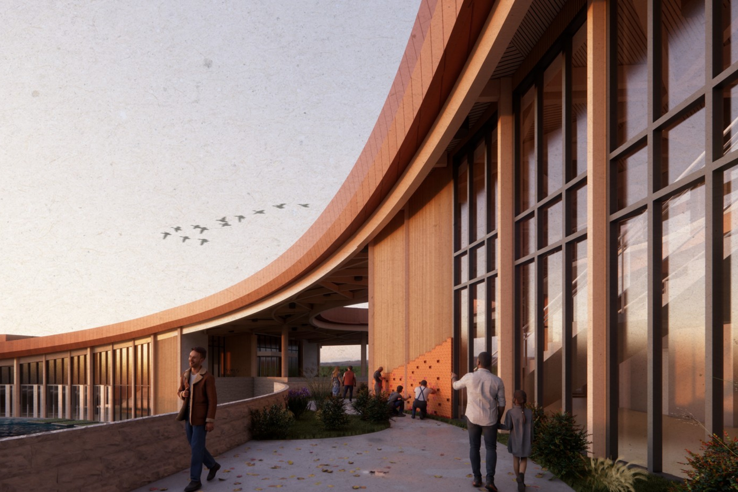 Curved modern building with large windows reflecting sunset.