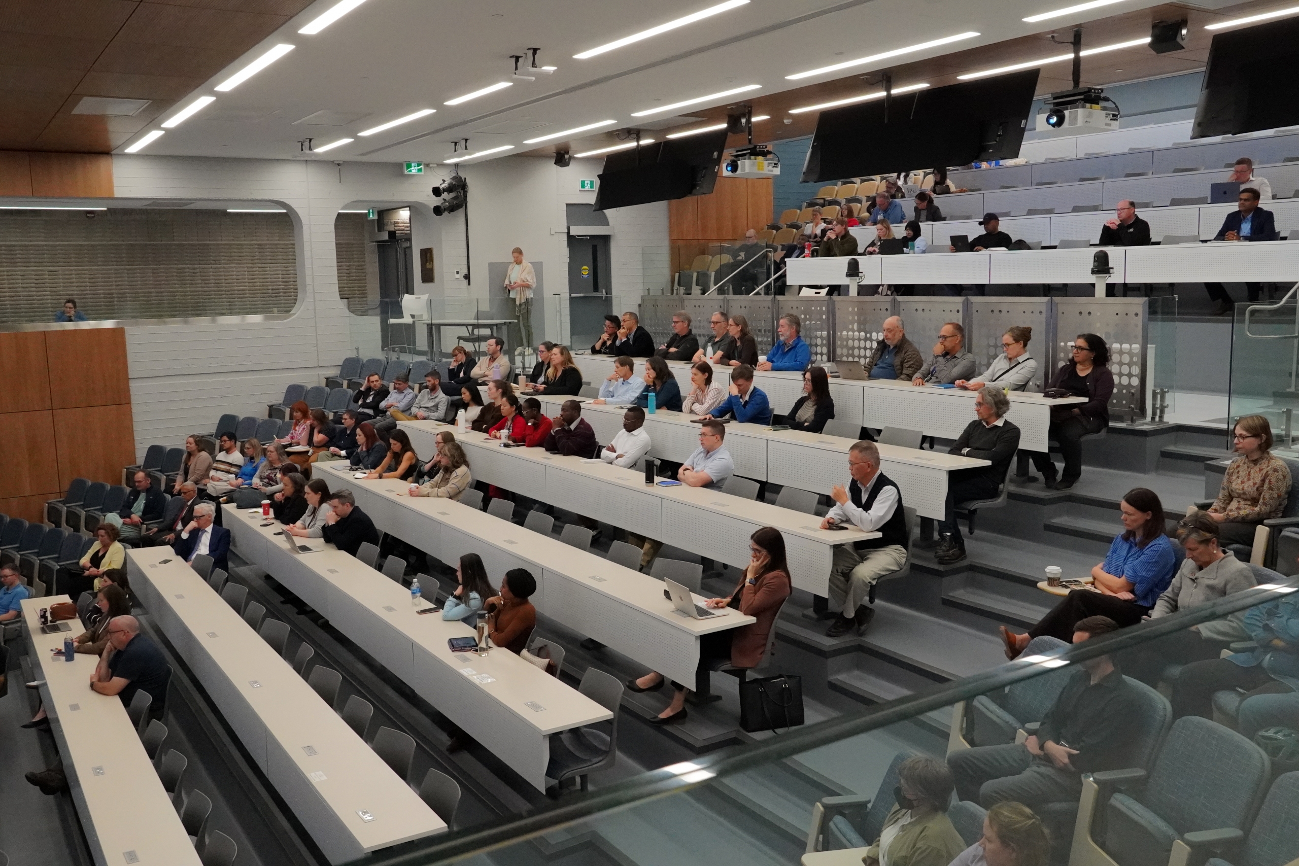 Audience of researchers and students seated in rows, listening to a speaker at the front of a room.