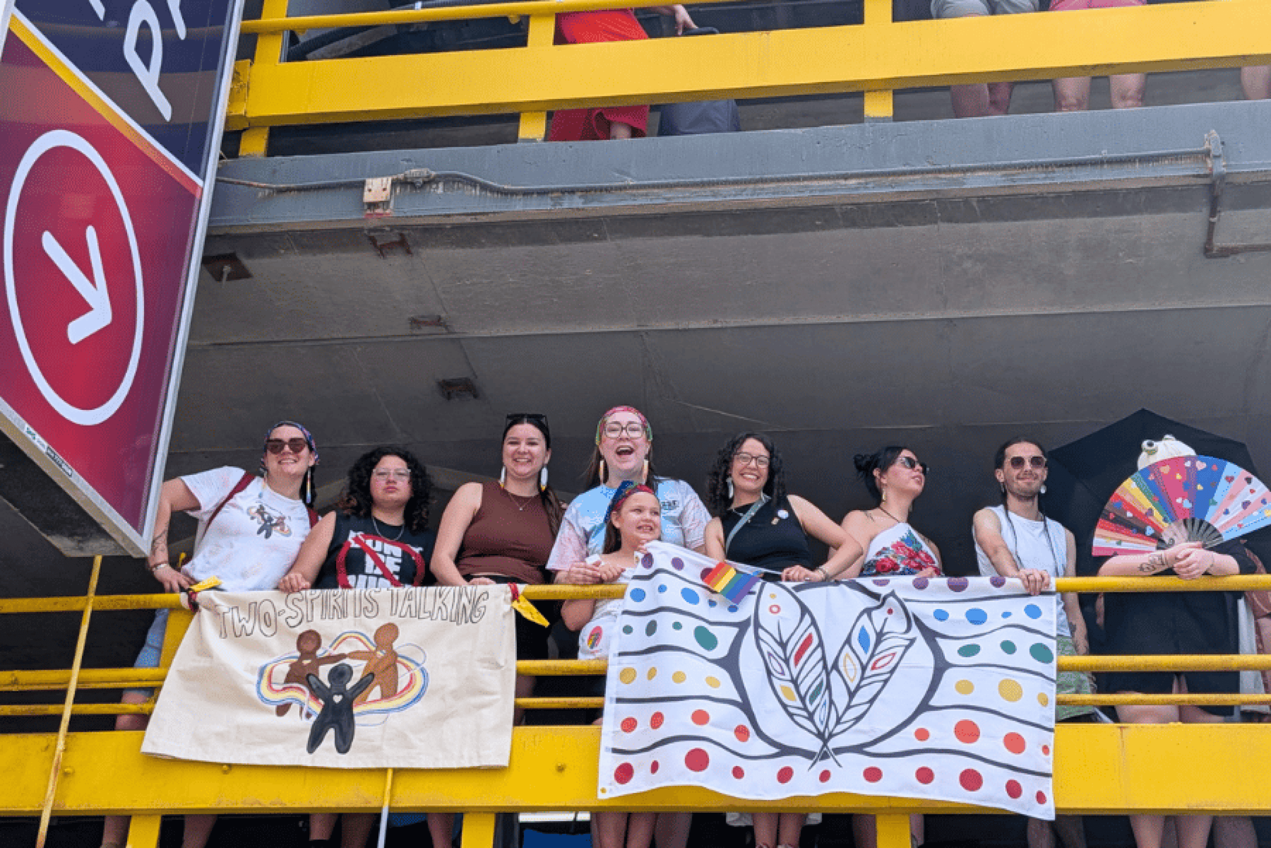 Two-Spirits Talking members pose with community banners during a Pride celebration.