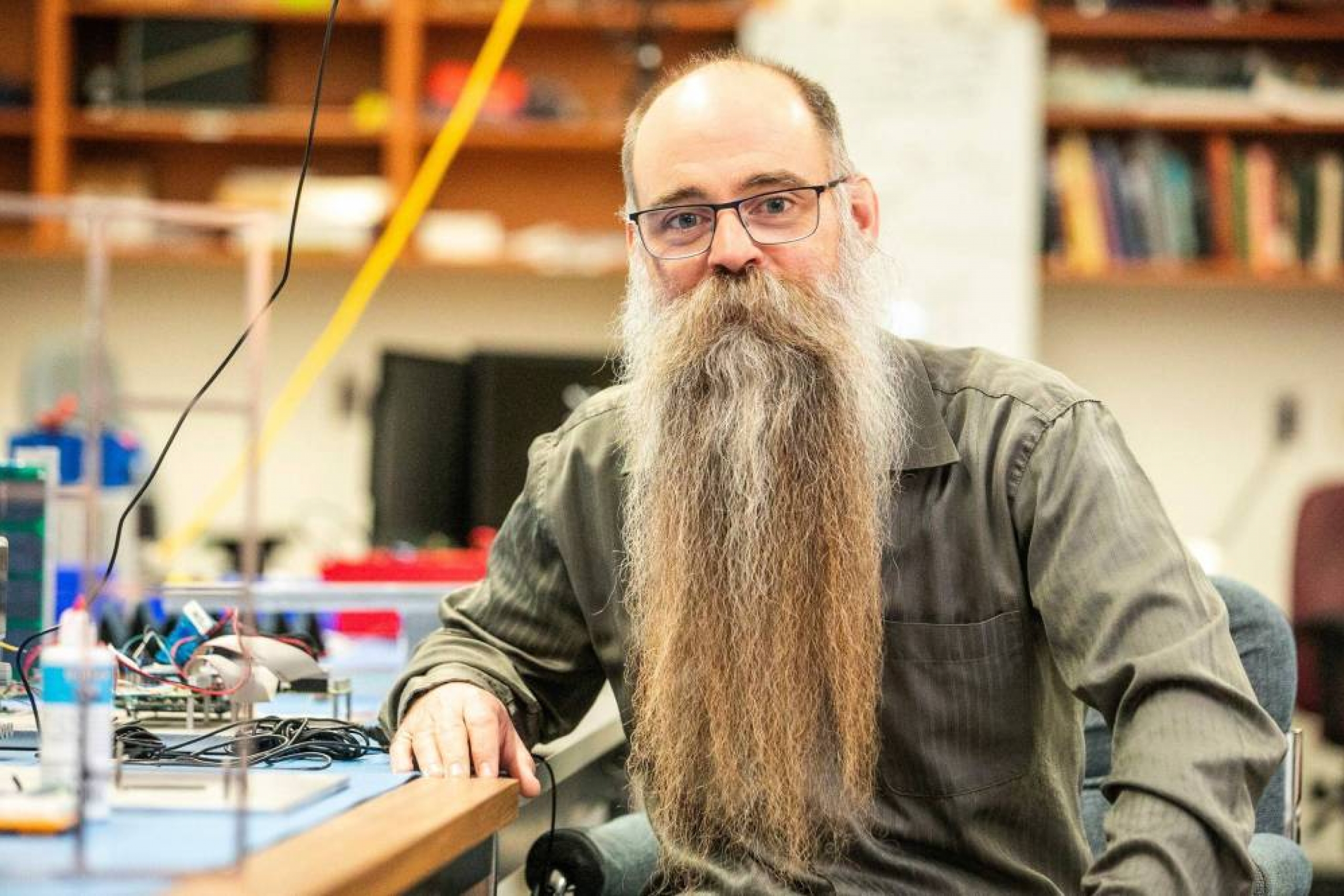 Dr. Philip Ferguson, wearing glasses and sporting a long beard, seated in a laboratory surrounded by research equipment