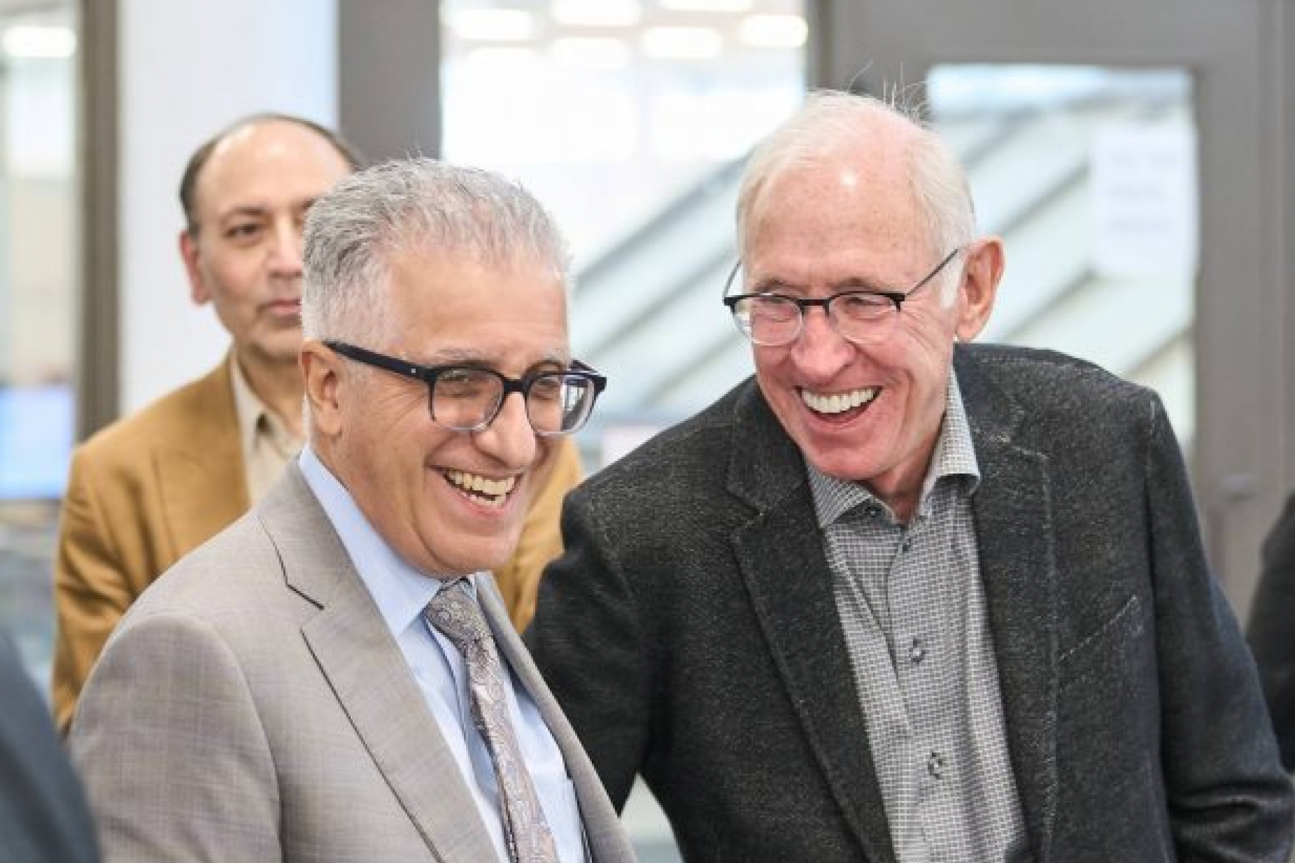 Two men, each dressed in suits, stand side by side with happy expressions