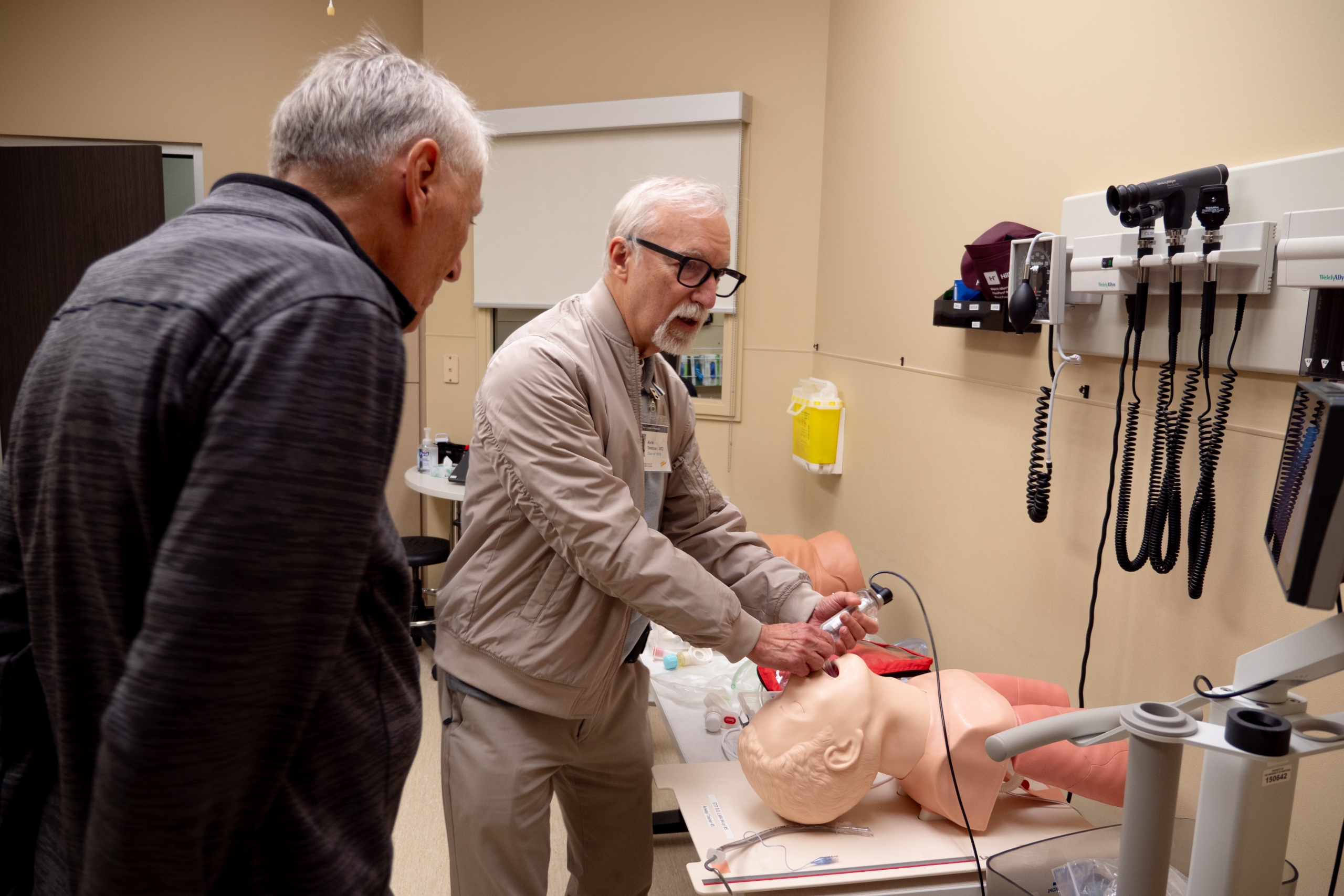 Two medicine alumni use a training manikin. 