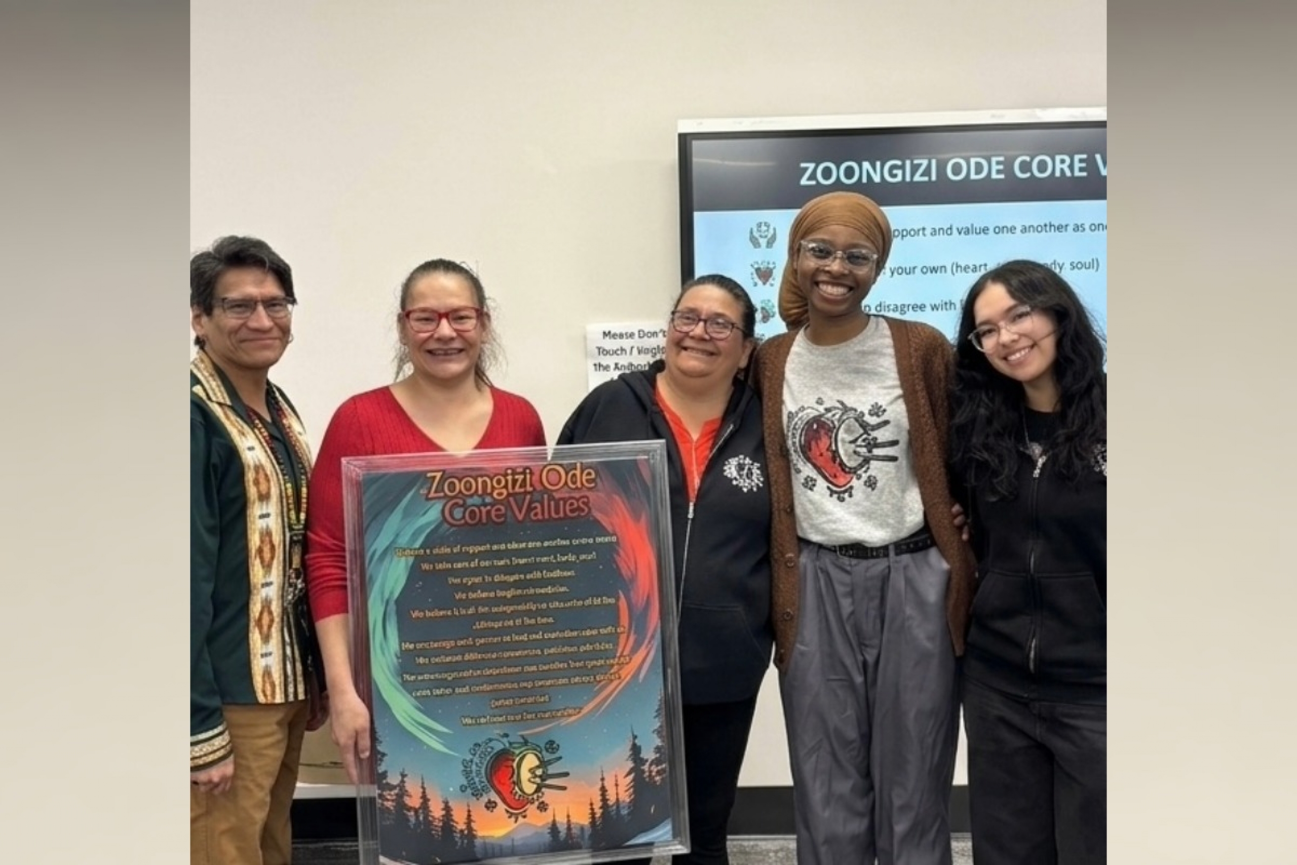 Five people smile at the camera. One person holds a poster with Zoongizi Ode core values.
