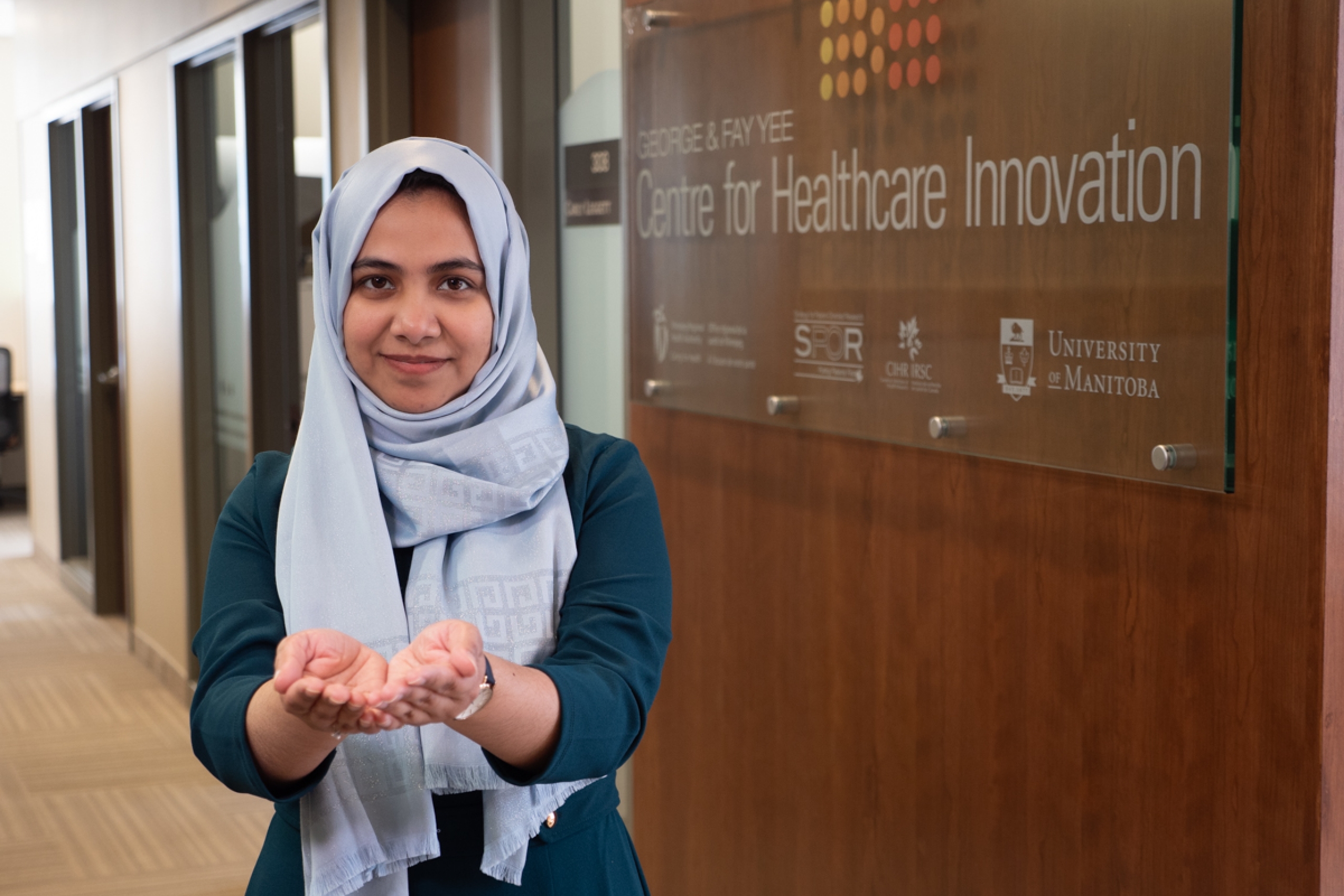 Nasiba Ahmed strikes the Give to Gain pose, beside her is a Centre for Healthcare Innovation signage.