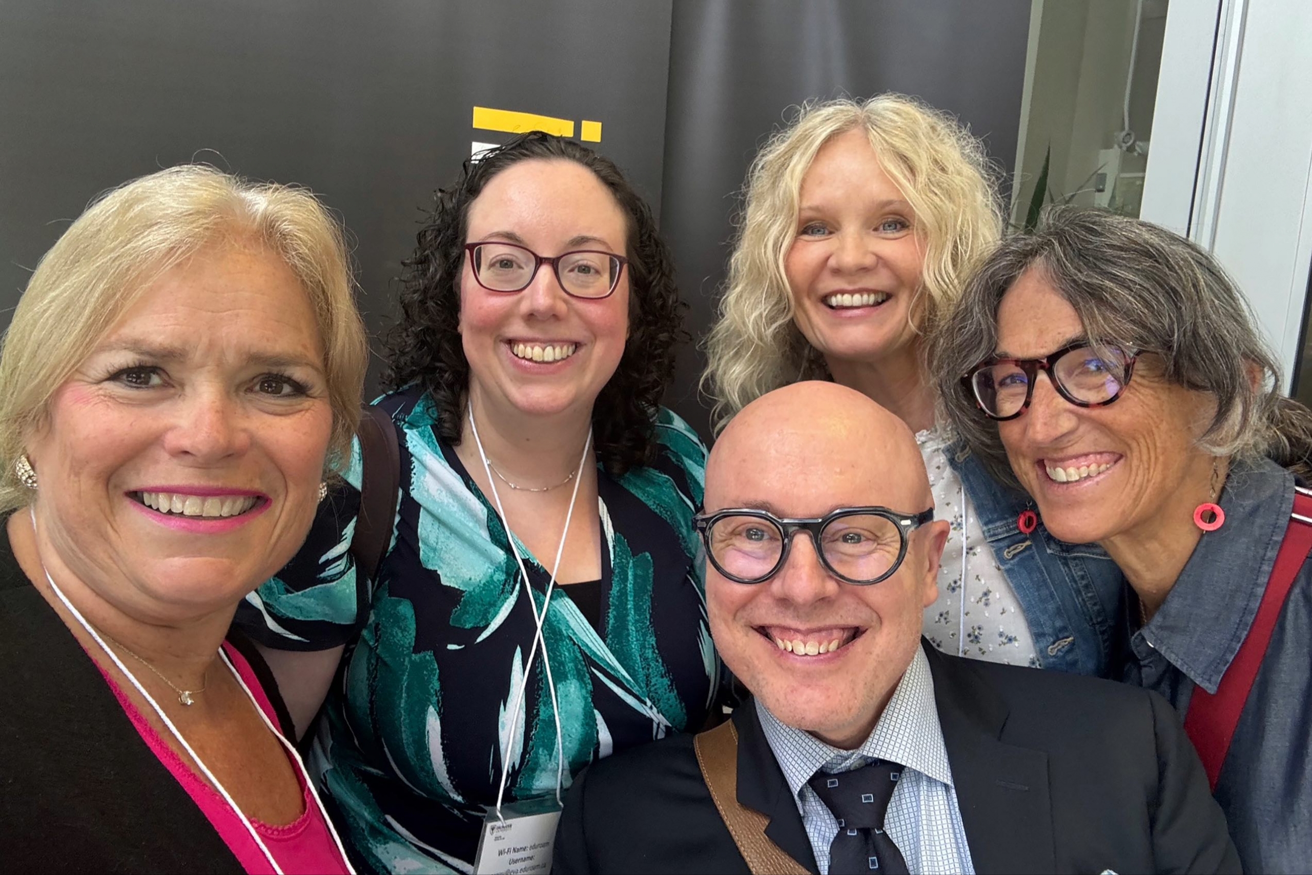 five people smile at the camera clustered together for a selfie