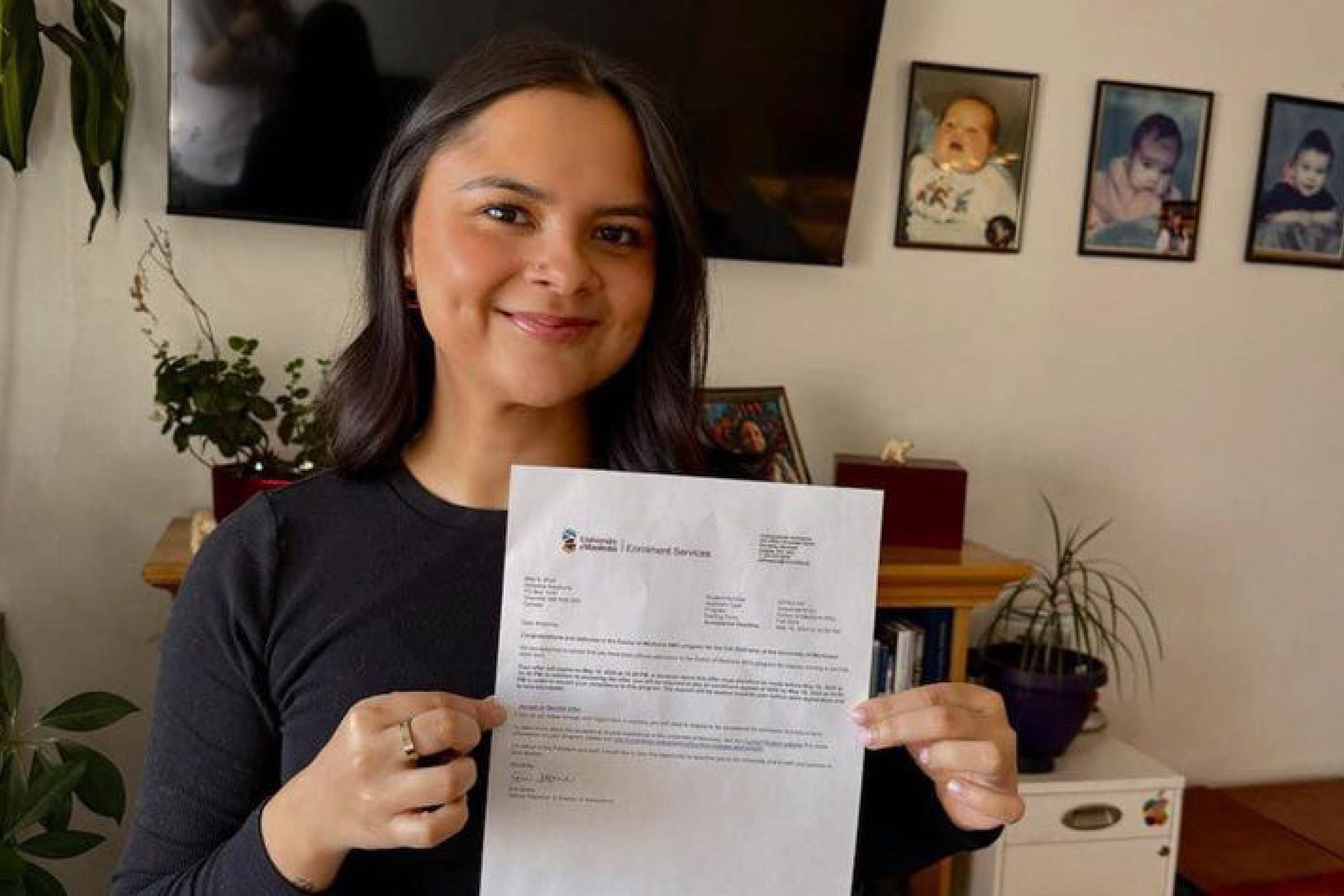 A woman holds up her medical school entry letter and smiles