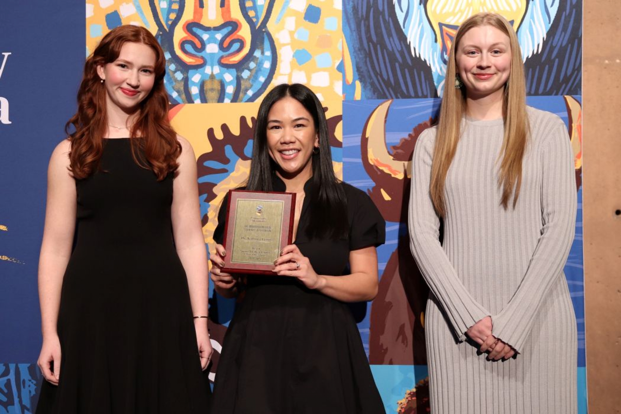 Three people pose for photo. One is holding a plaque. 