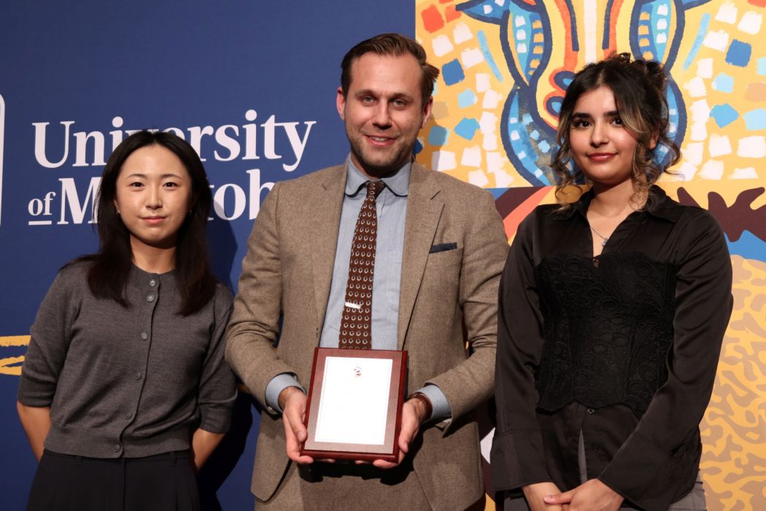 Three people pose for photo. One is holding a plaque. 