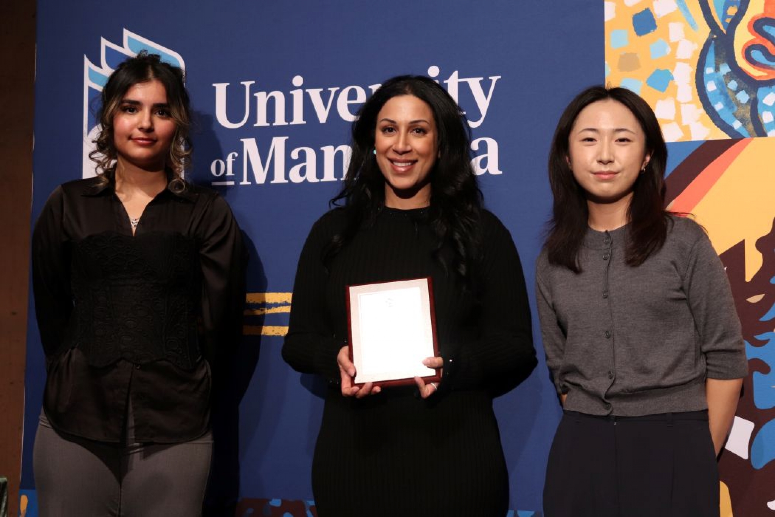 Three people pose for photo. One is holding a plaque. 
