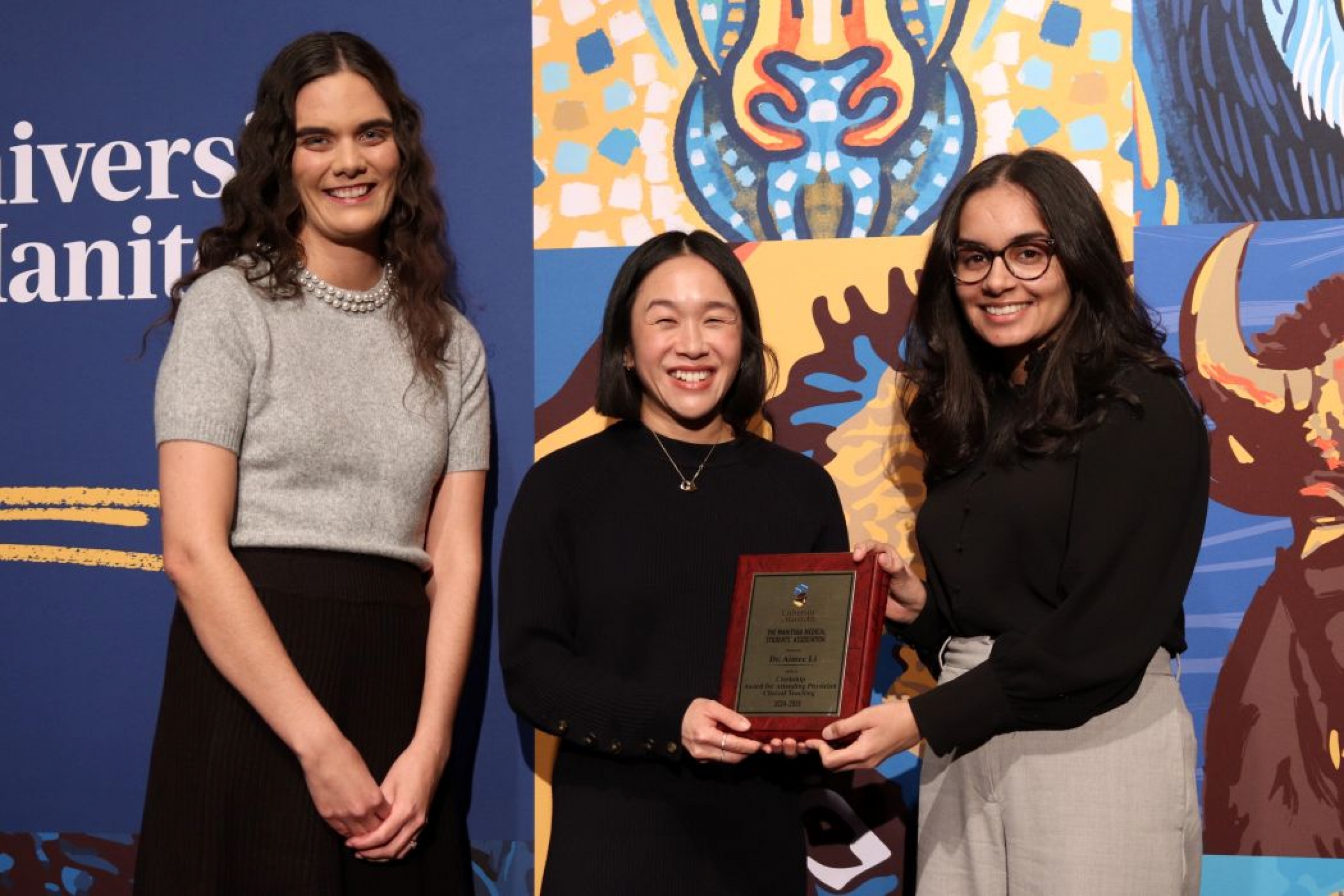 Three people pose for photo. One is holding a plaque. 