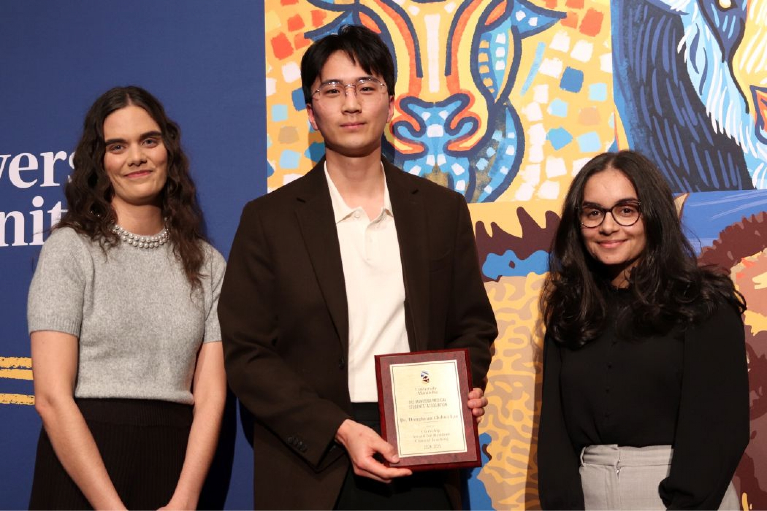 Three people pose for photo. One is holding a plaque. 