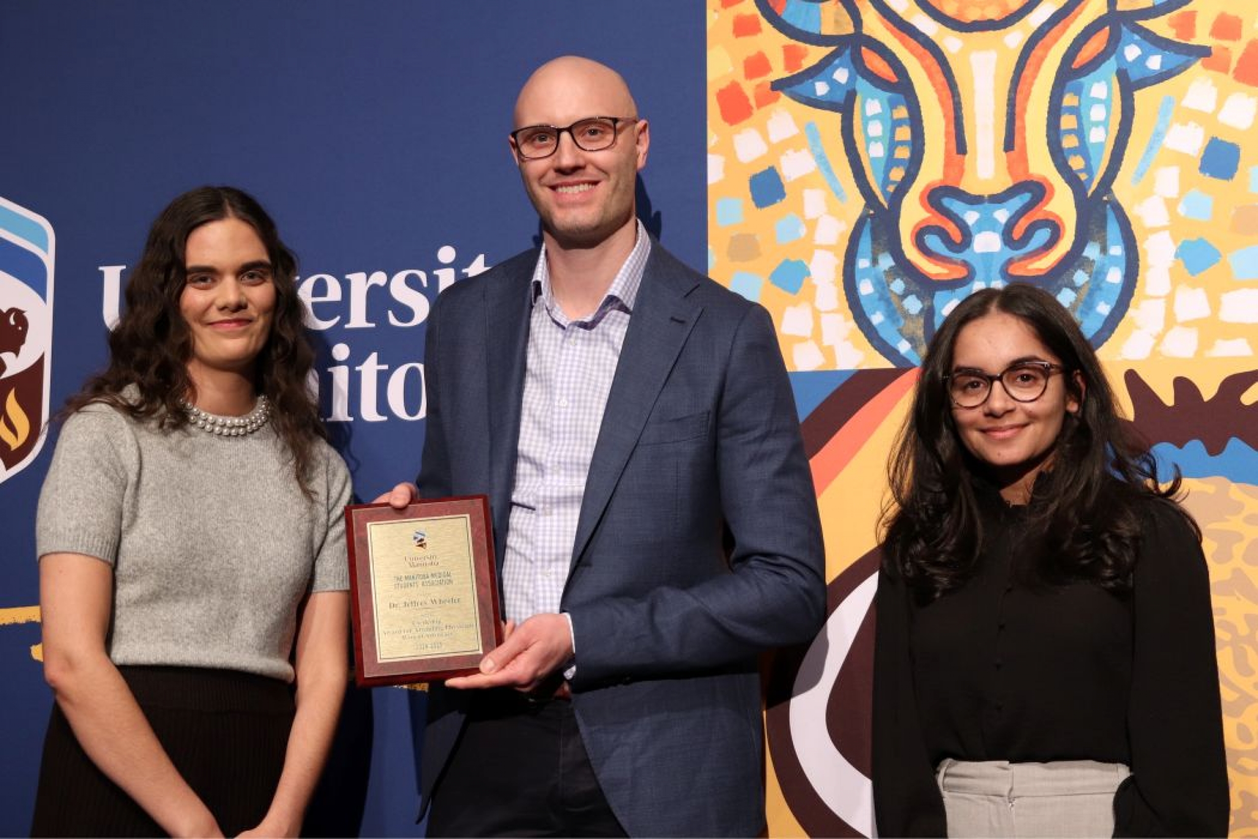 Three people pose for photo. One is holding a plaque. 