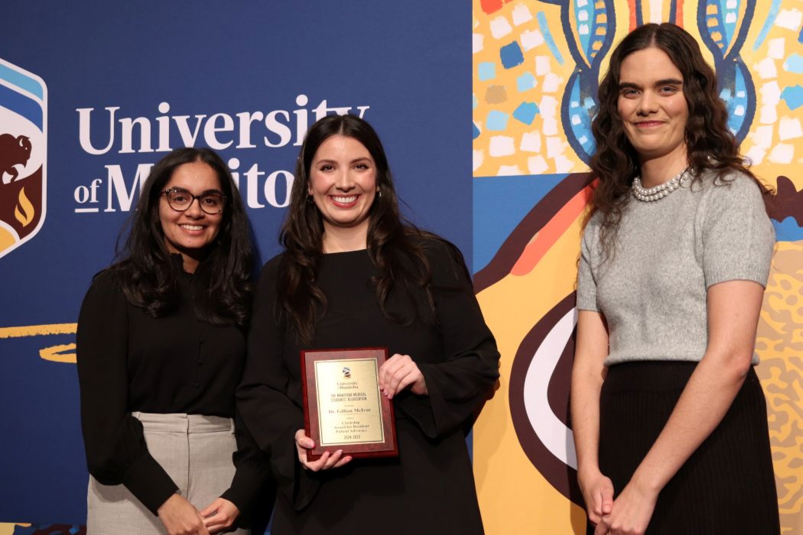 Three people pose for photo. One is holding a plaque. 