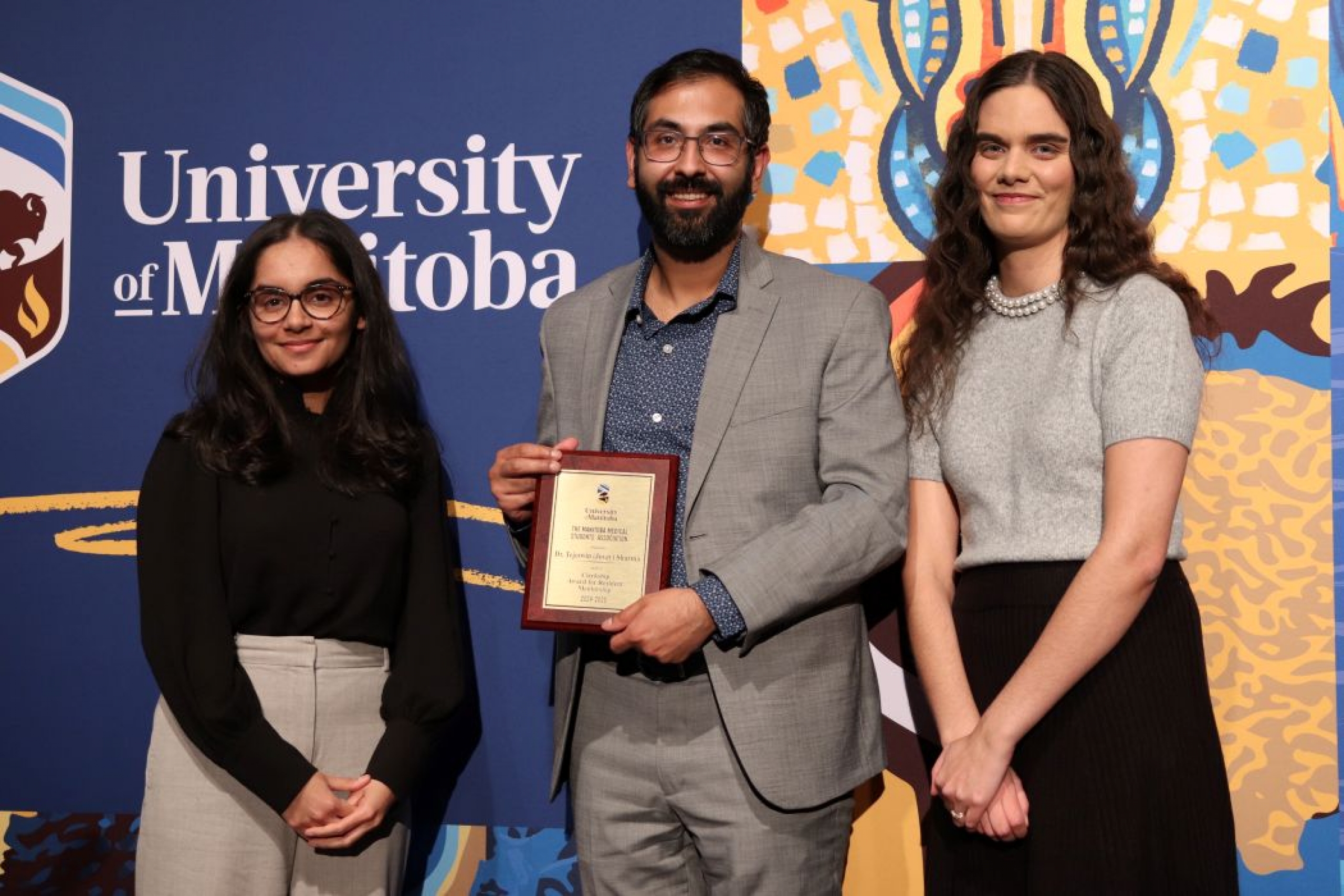 Three people pose for photo. One is holding a plaque. 