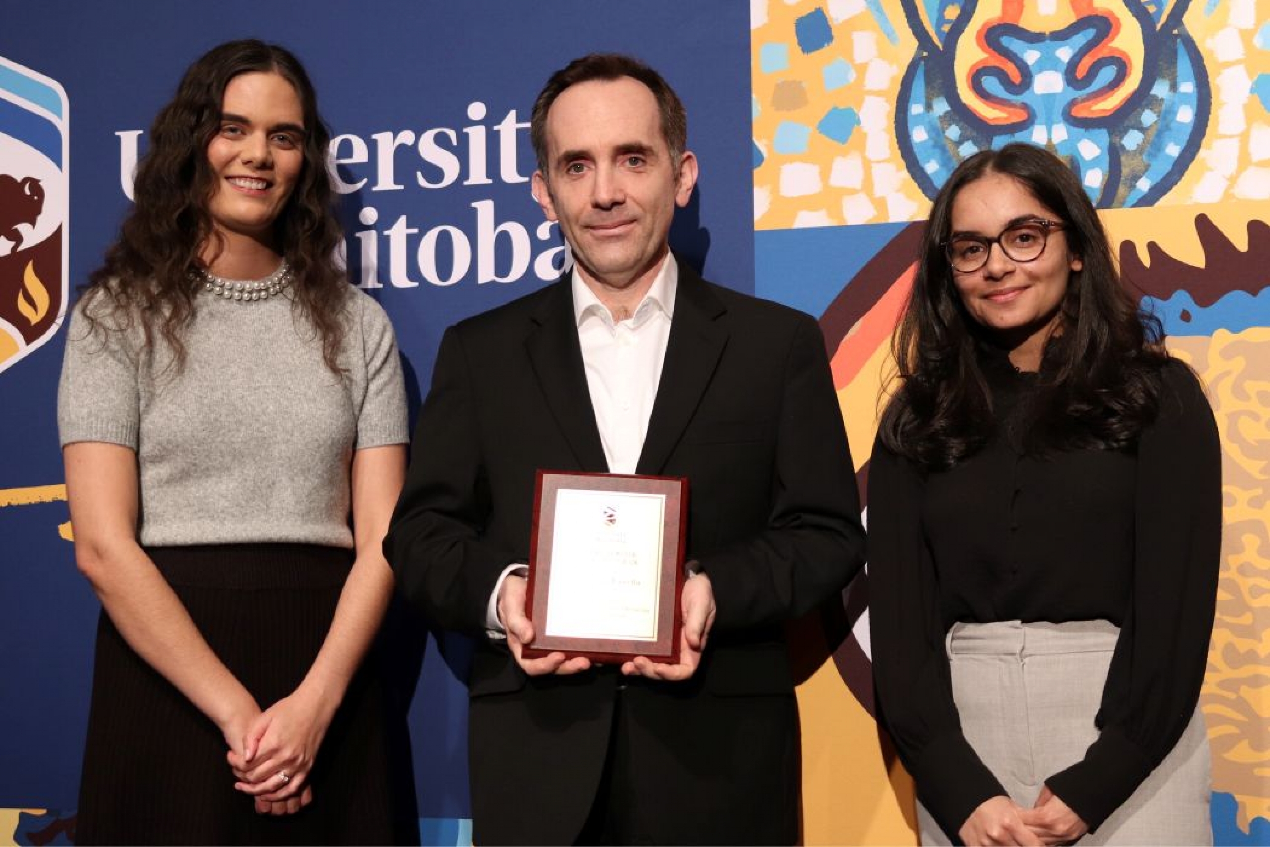 Three people pose for photo. One is holding a plaque. 