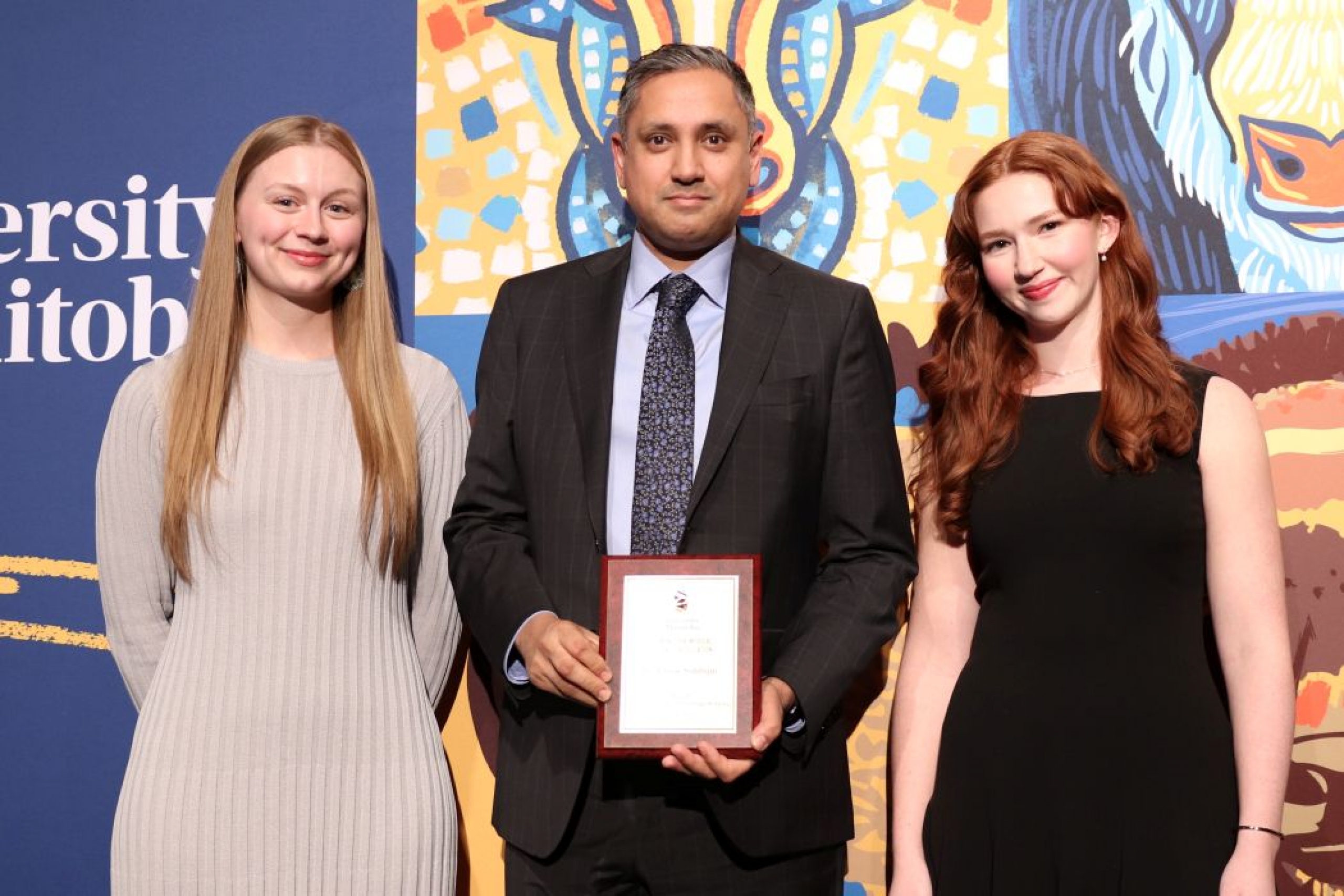 Three people pose for photo. One is holding a plaque. 
