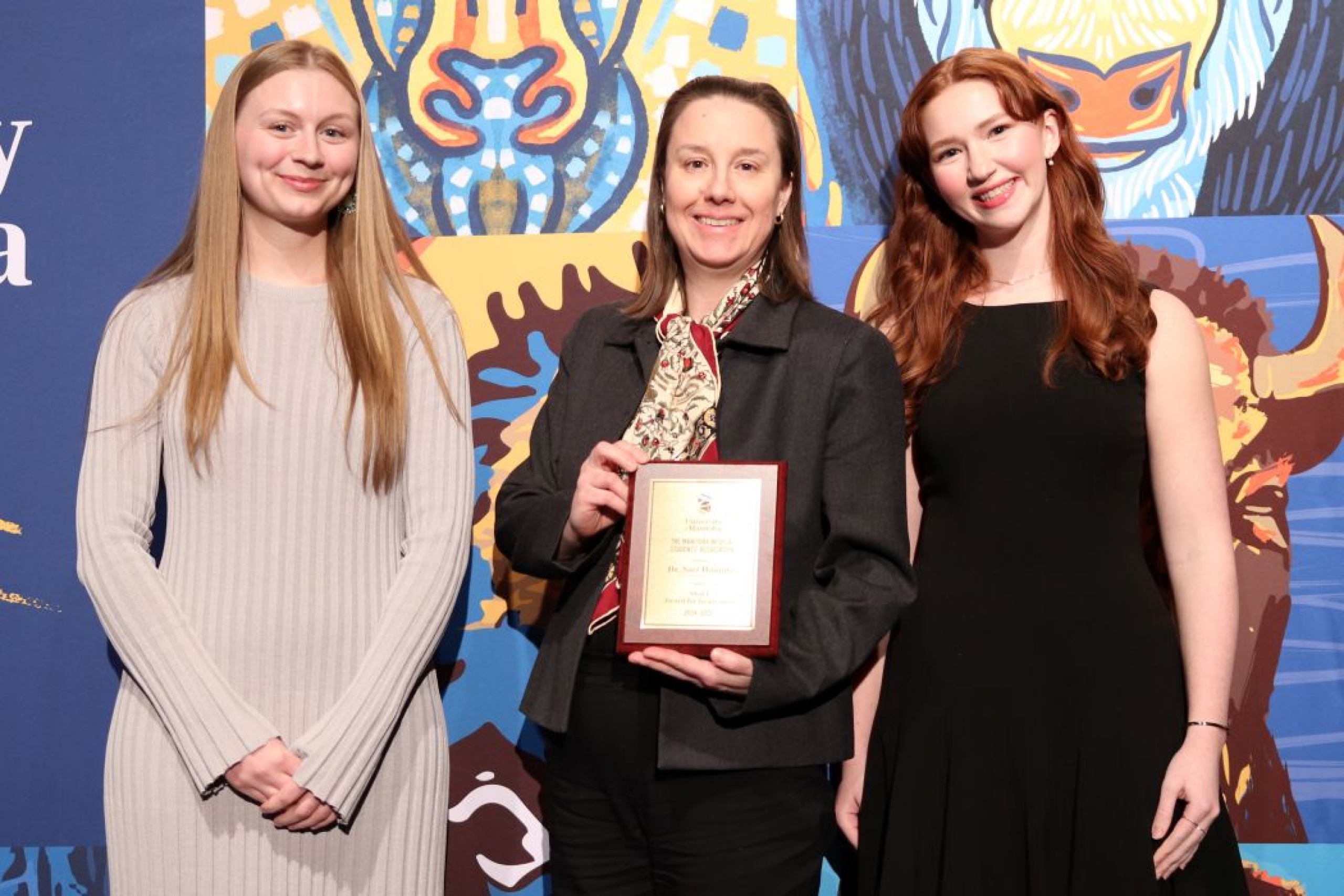 Three people pose for a photo. One is holding a plaque.