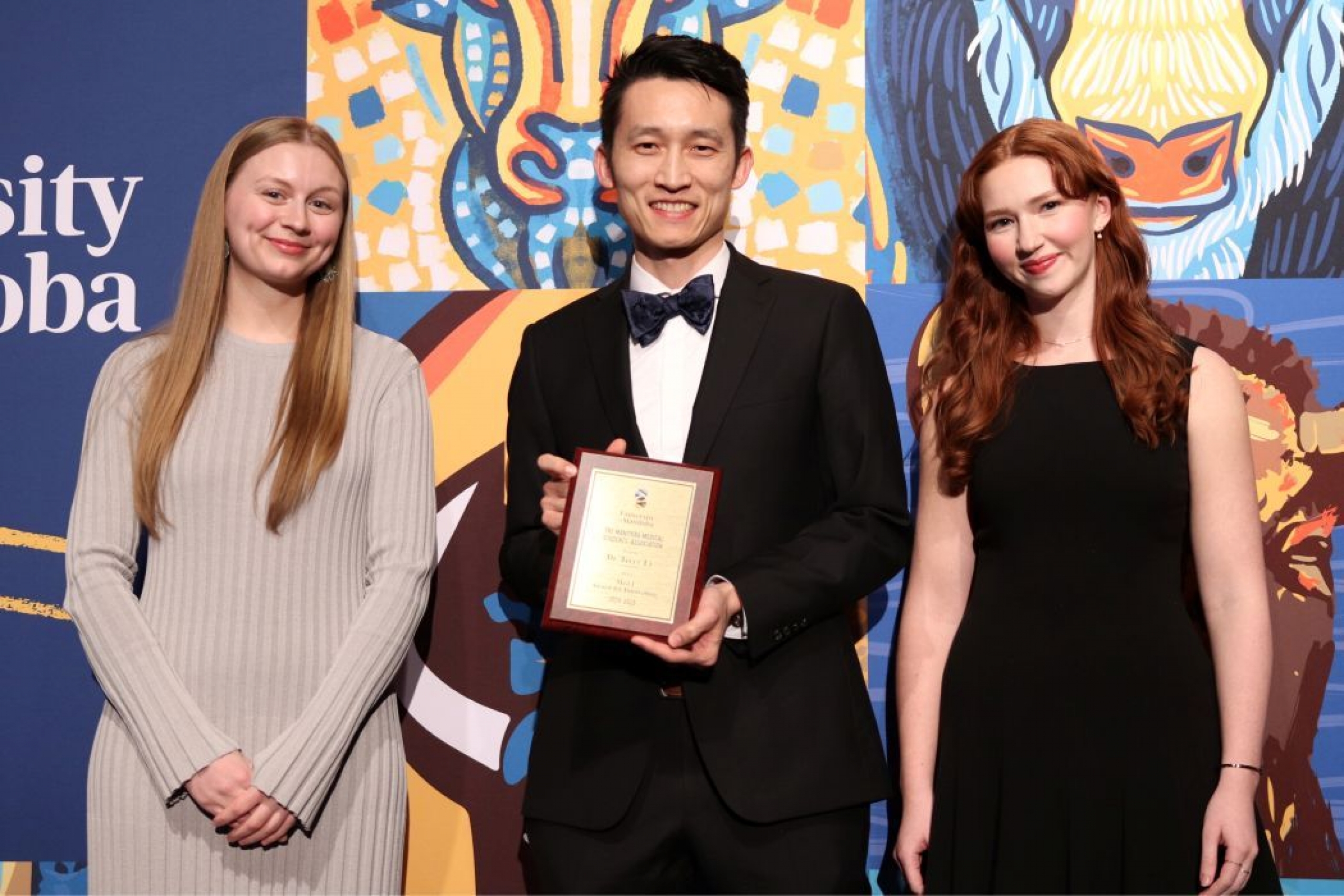 Three people pose for photo. One is holding a plaque. 