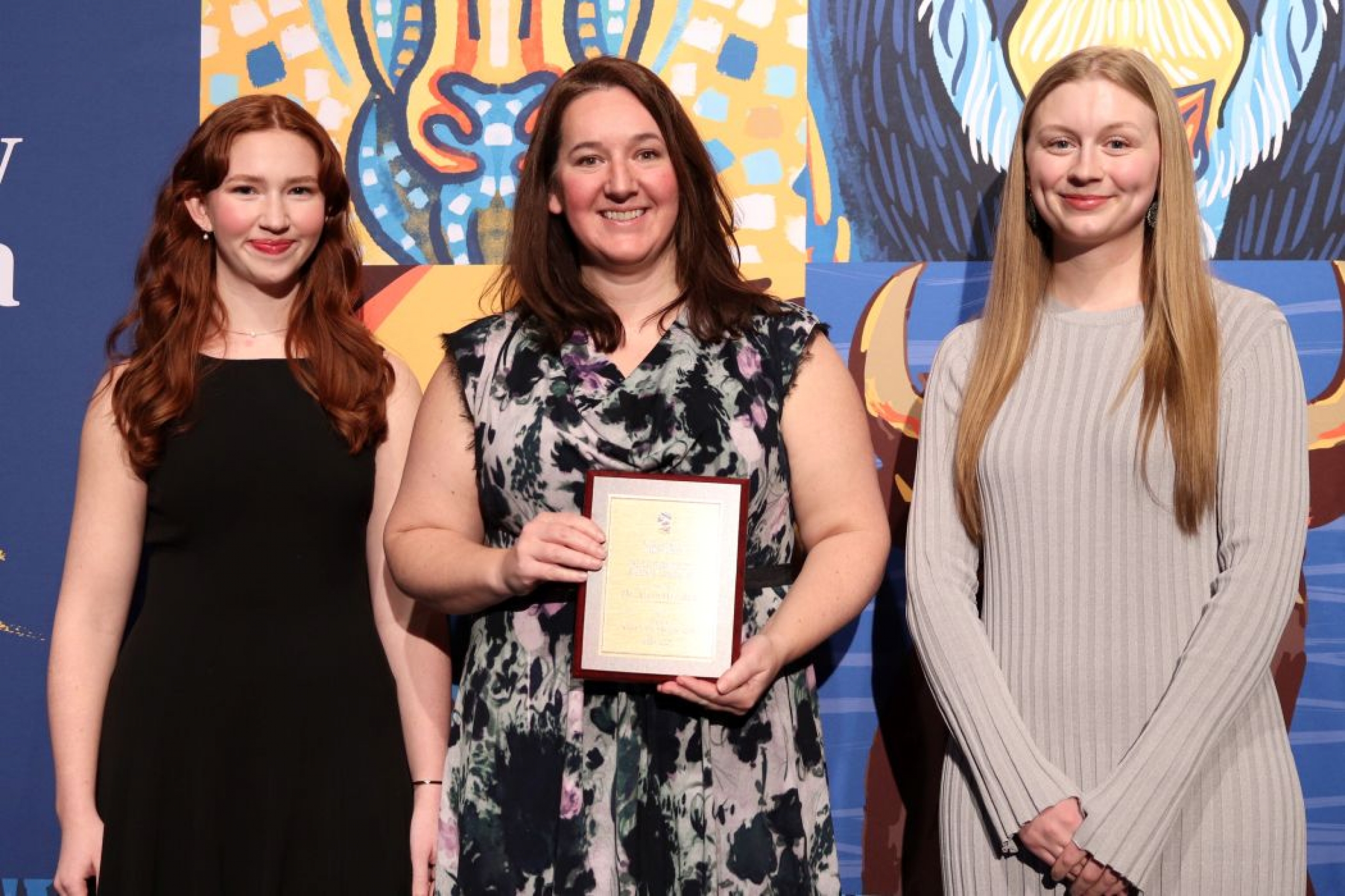 Three people pose for photo. One is holding a plaque. 