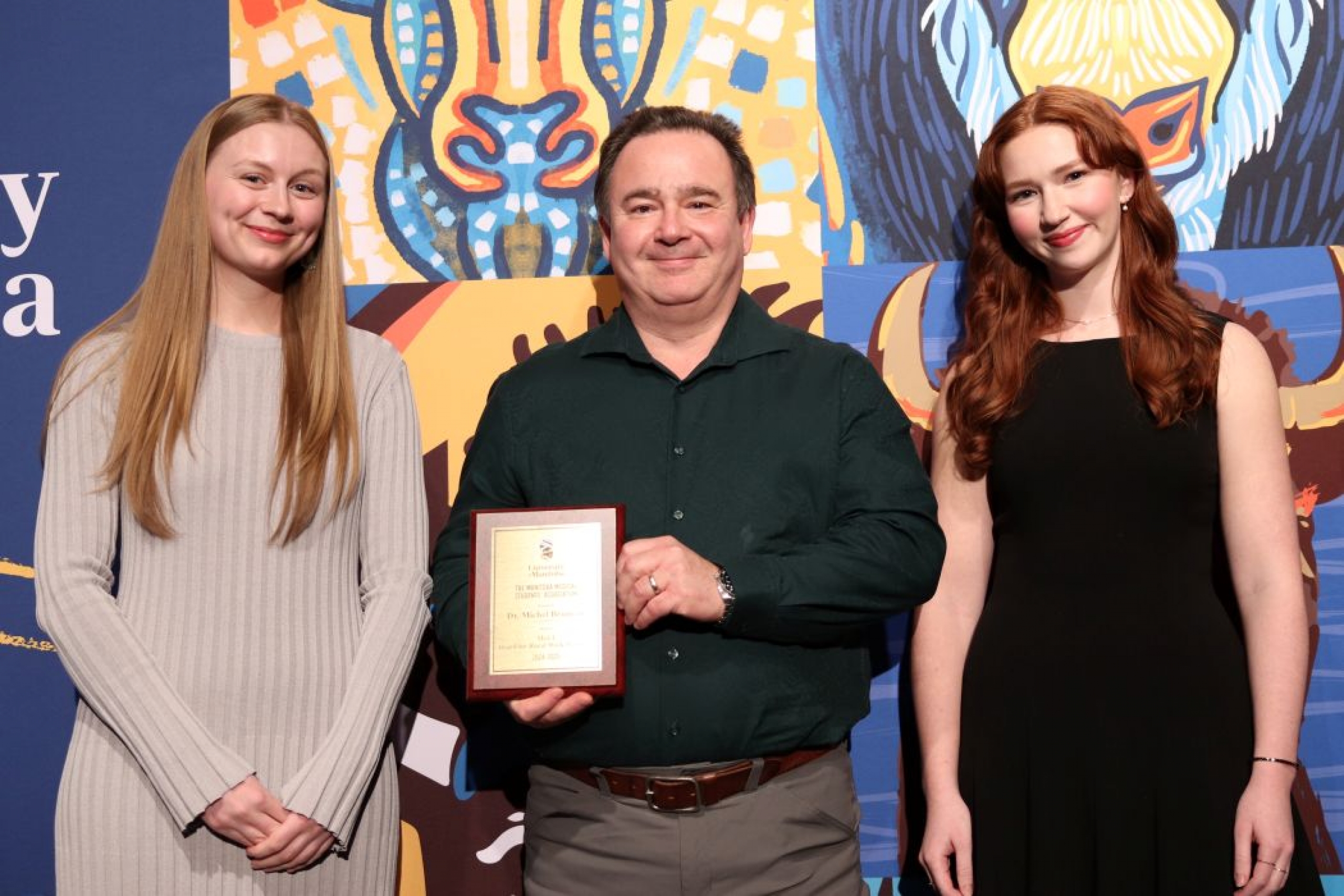 Three people pose for photo. One is holding a plaque. 