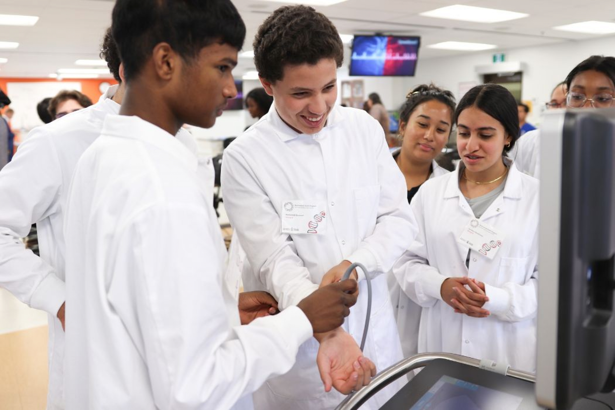 Group of campers in lab coats during a medical workshop; one camper receives a wrist ultrasound while another holds the ultrasound probe.