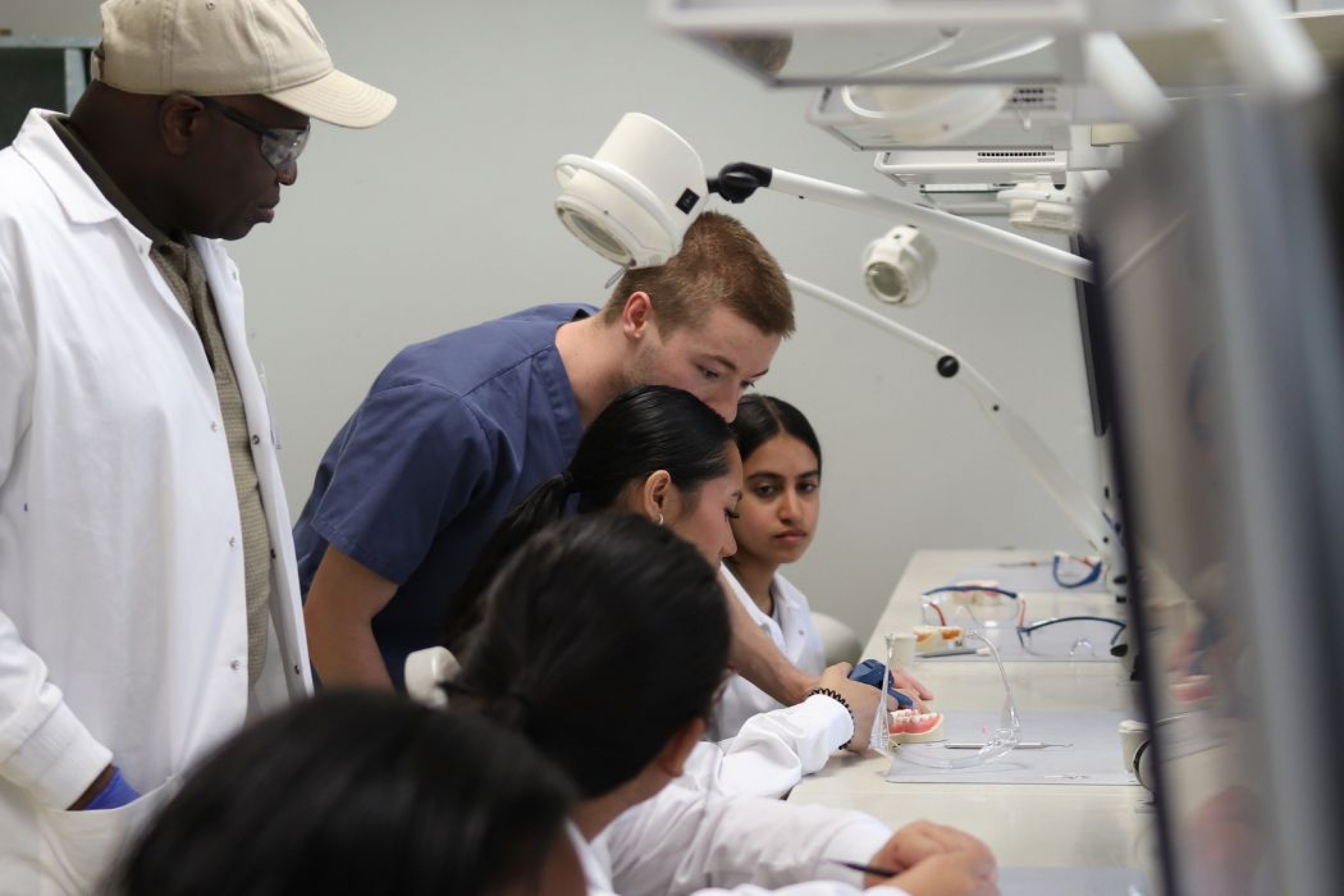 Two instructors guide students in a dentistry lab as they examine dental models.